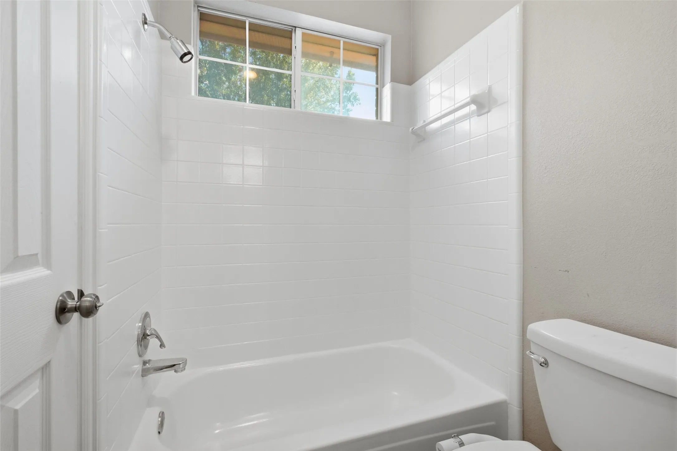 The Jack and Jill's  bath's tub/shower combo features a white subway tile surround, a window above the tub for natural light, and brushed nickel fixtures — fresh, clean, and fully functional for everyday use