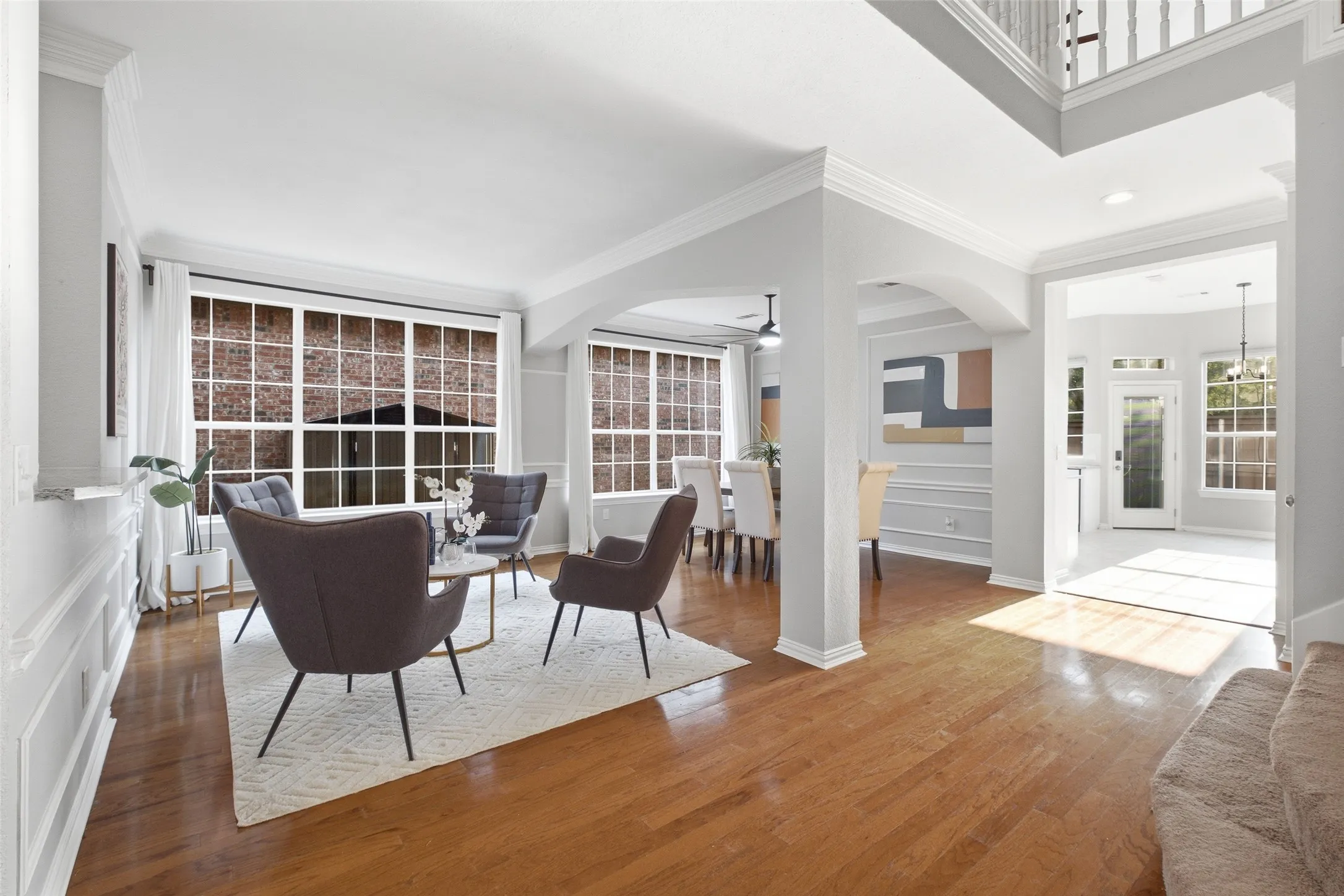 Rich hardwood floors, elegant board-and-batten wainscoting, and a wall of windows define the formal living room just off the foyer. Arched passageways connect this space to both the dining room and the main hallway, creating a natural flow for entertaining.
