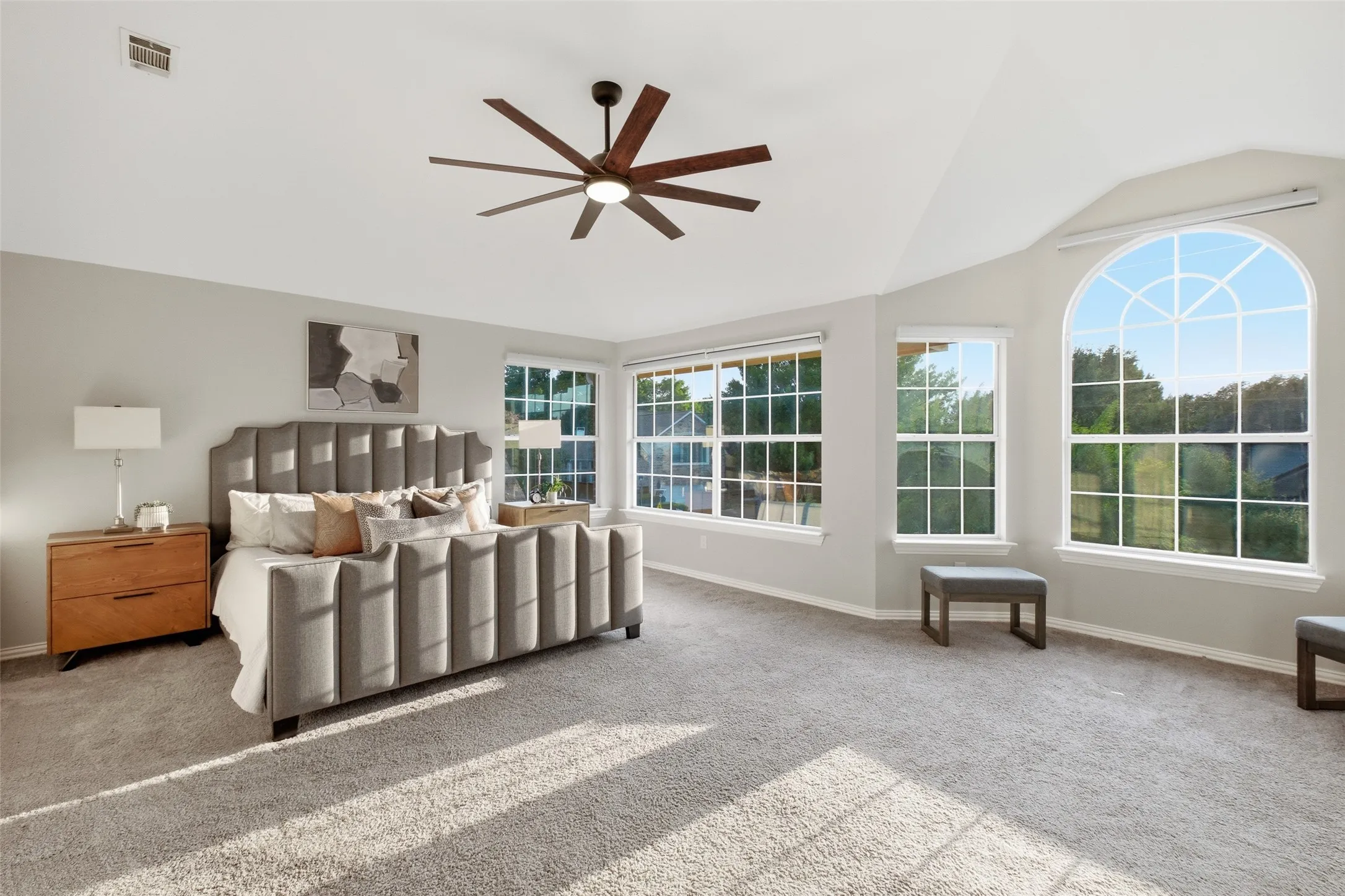 Privately tucked at the back of the second floor, the primary bedroom is truly oversized — vaulted ceilings, an eight-blade statement ceiling fan, plush carpet, and a wall of windows including a dramatic arched window that fills the room with treetop views. There's ample room for a king-sized bed plus a separate sitting area.
