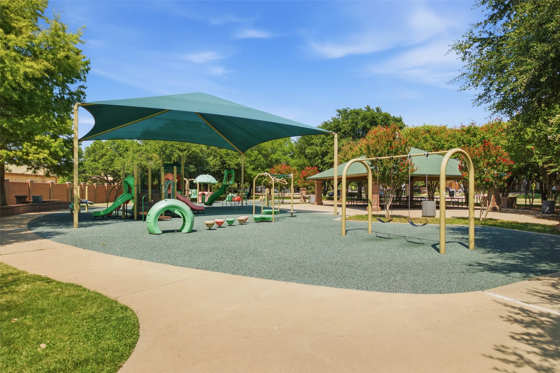 Les Lacs Park features a full playground with shade sails, slides, swings, and rubber safety surfacing, plus a picnic pavilion surrounded by blooming crape myrtles. A top-tier neighborhood park, all within walking distance.