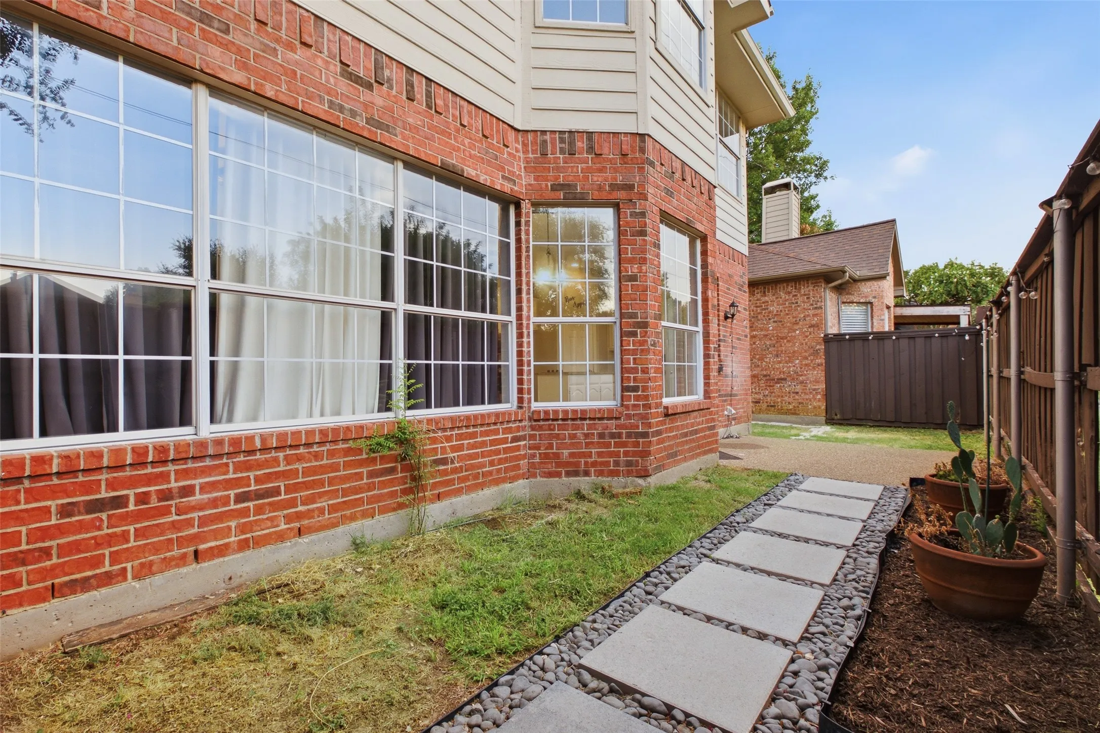 The back of the home showcases the oversized windows that bring so much natural light into the family room and kitchen. The patio, stepping stone paths, and fenced yard complete a private, well-landscaped outdoor retreat.
