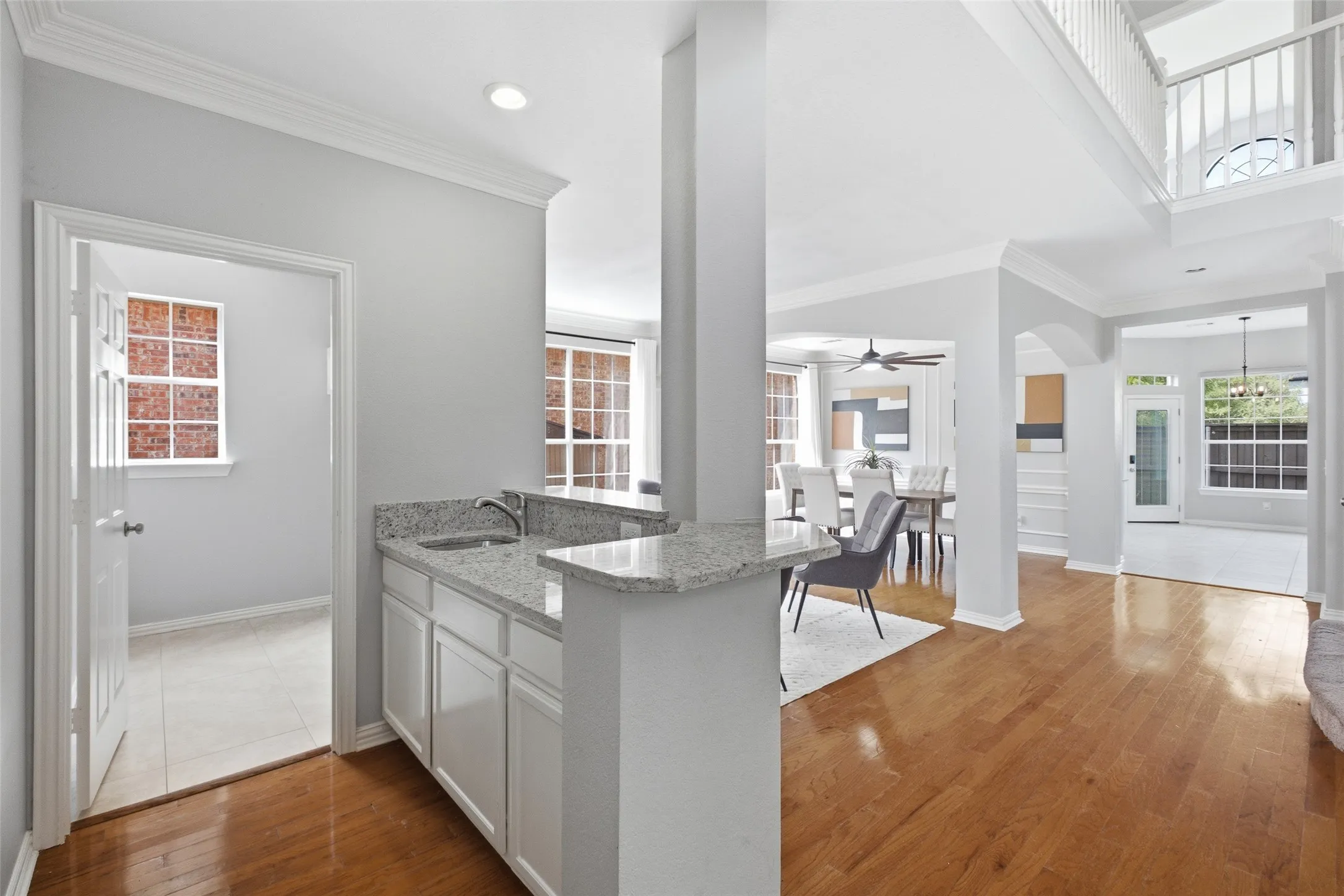 A granite-topped wet bar with sink provides the perfect pass-through between the kitchen and the formal spaces — ideal for entertaining. The view opens through to the foyer and the two-story entry beyond, adding an impressive sense of scale.
