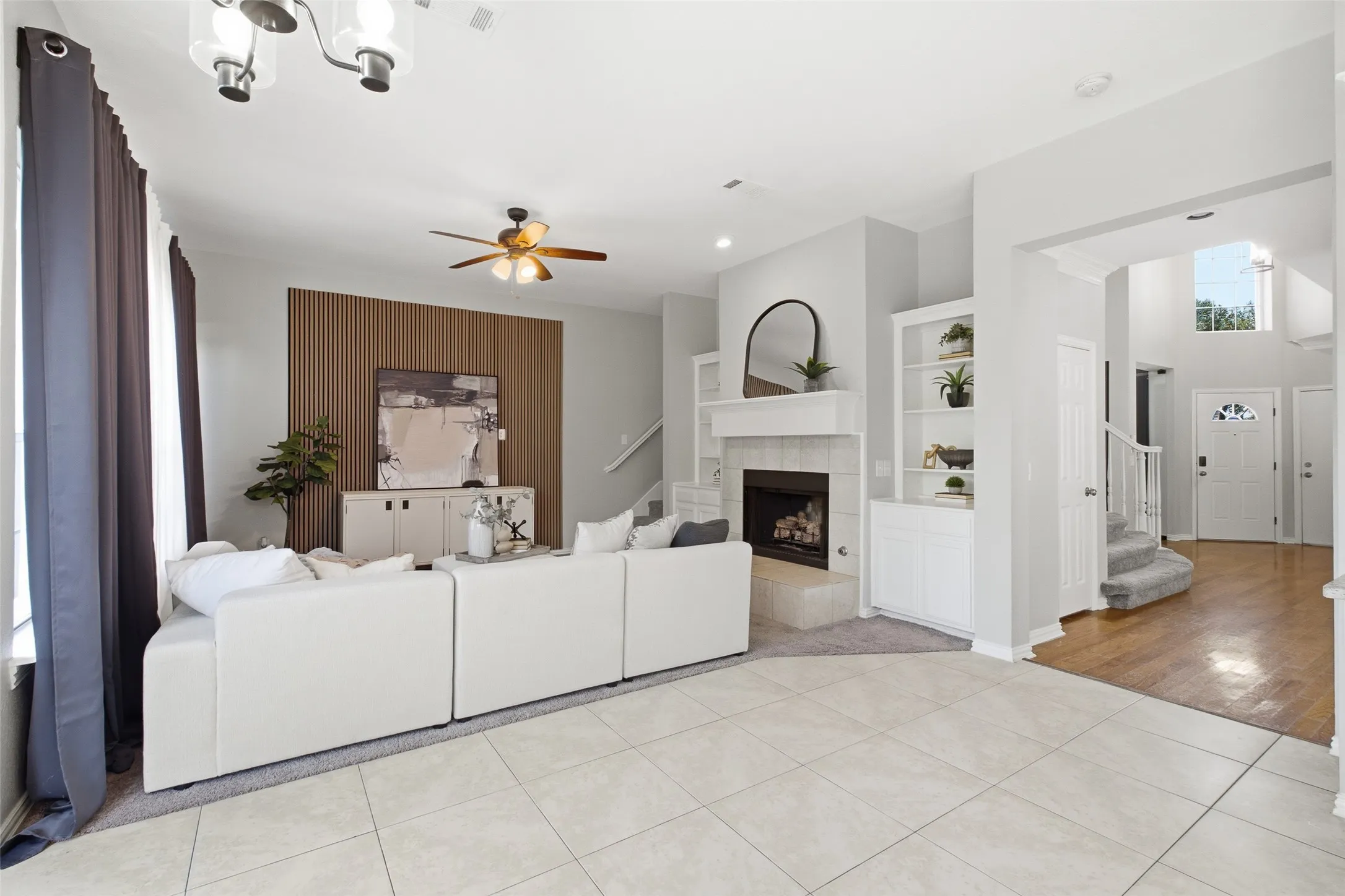 The expansive main level reveals just how much space this home delivers — family room, built-ins, fireplace, and the gracious foyer with its grand staircase all visible in one sweeping view. Tile flooring transitions to rich hardwood as the rooms connect seamlessly from front to back.
