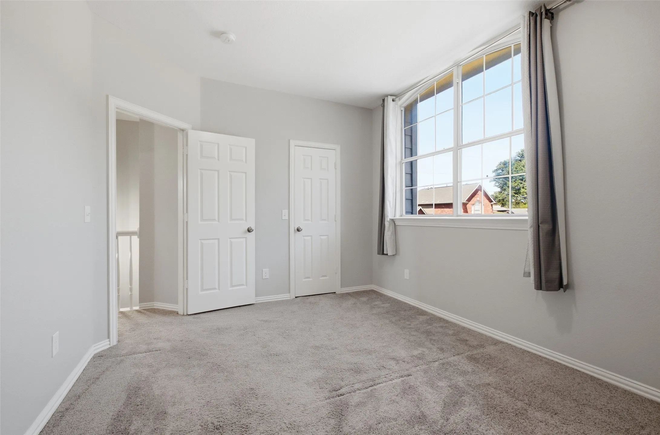 A bright front-facing secondary bedroom with an arched-top window, two closet doors, plush carpet, and neutral walls — a clean canvas ready for any use.
