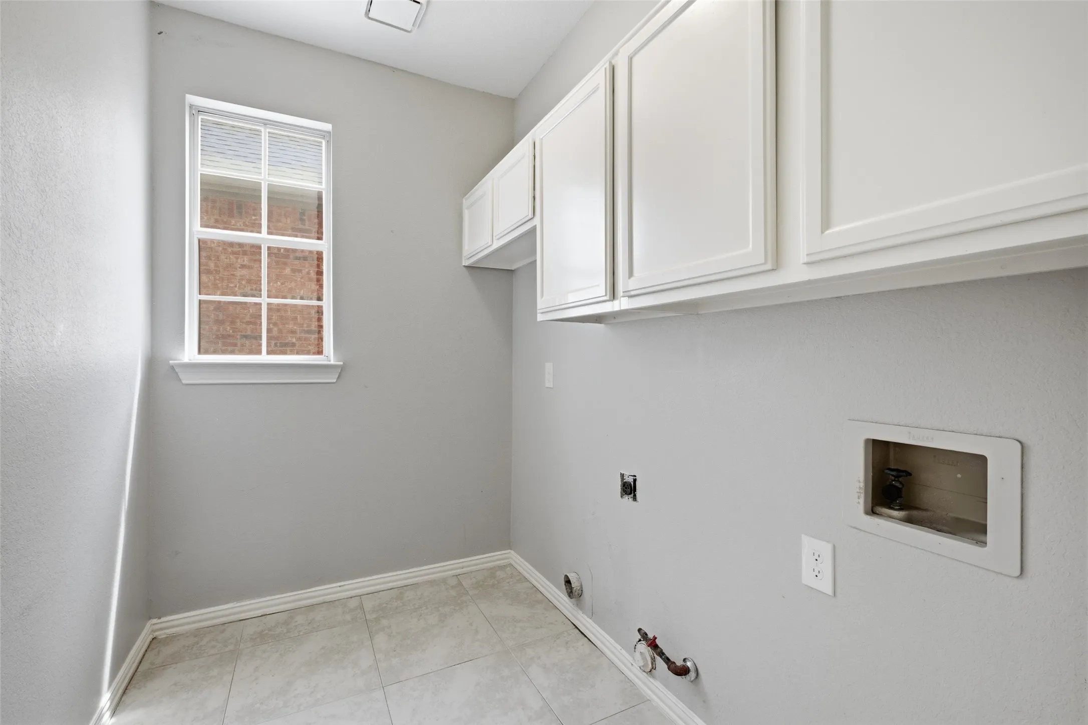 A dedicated laundry room on the main level offers white upper cabinetry for extra storage, tile flooring, a window for natural light, and full hookups for both electric and gas dryer. Practical, functional, and conveniently located off the kitchen.