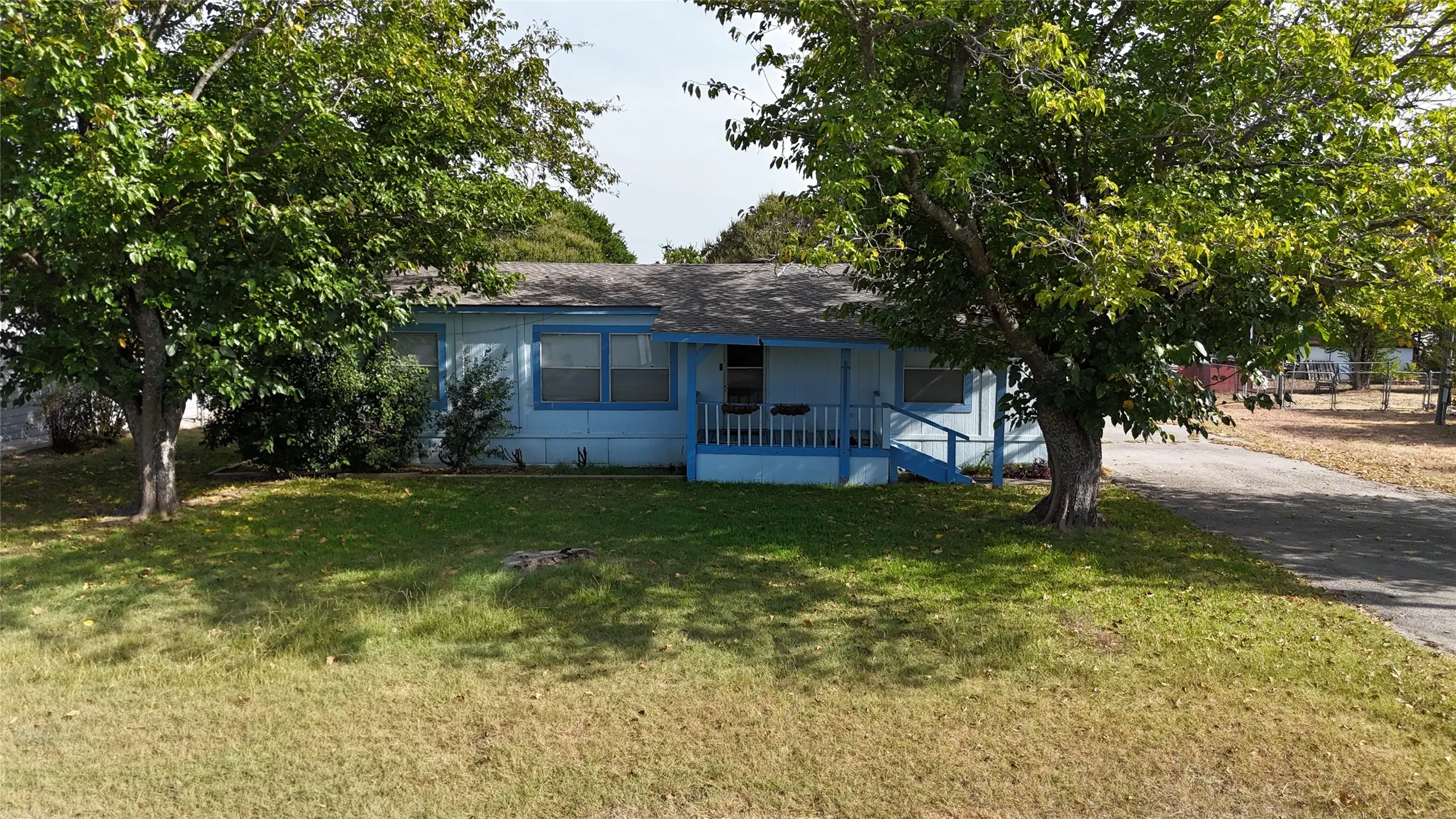 Single-story residence featuring a covered front porch with railings, a paved driveway, and mature landscaping