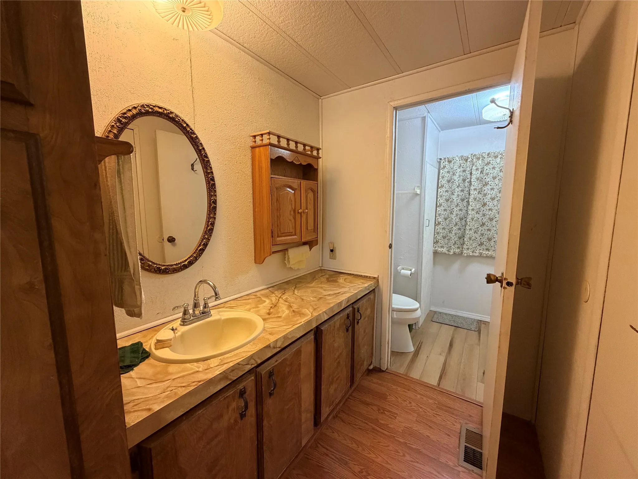 Vanity with integrated sink, expansive countertop, wood-finish cabinetry, and an ornate framed mirror