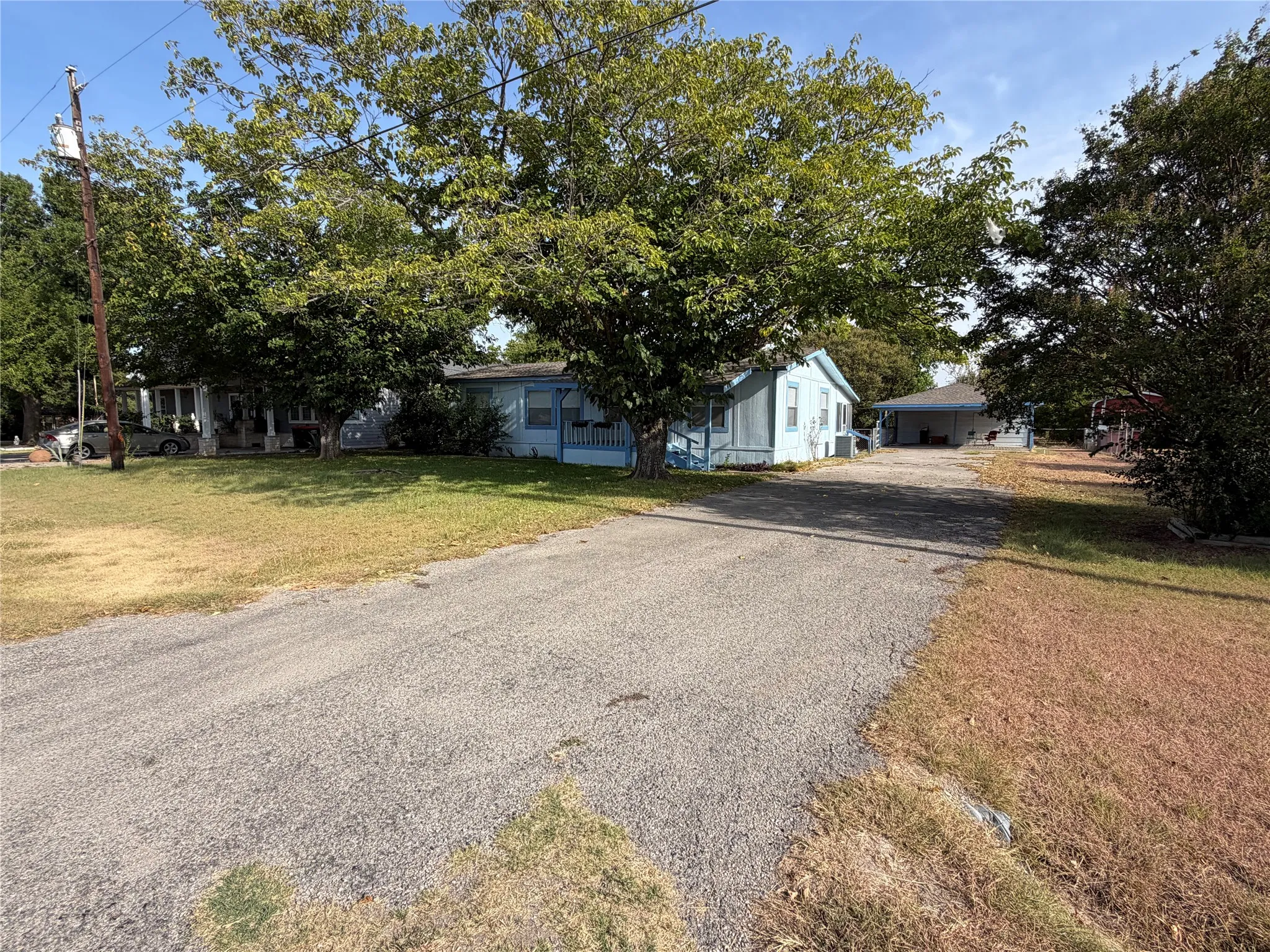 Gravel driveway leading to a blue exterior home with a covered front porch and mature trees