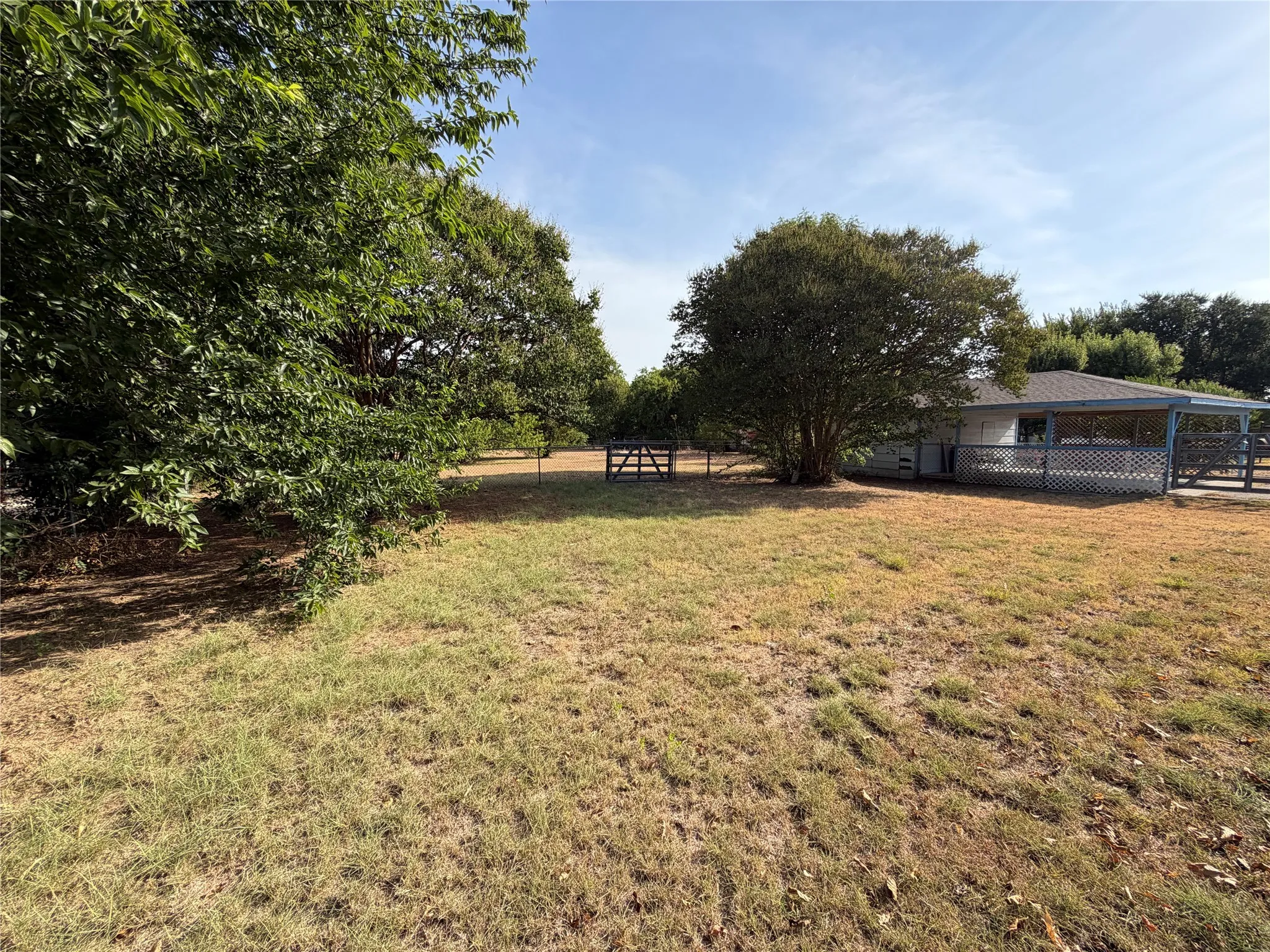 Expansive grounds featuring mature shade trees, open pasture, and rustic outbuildings with fencing