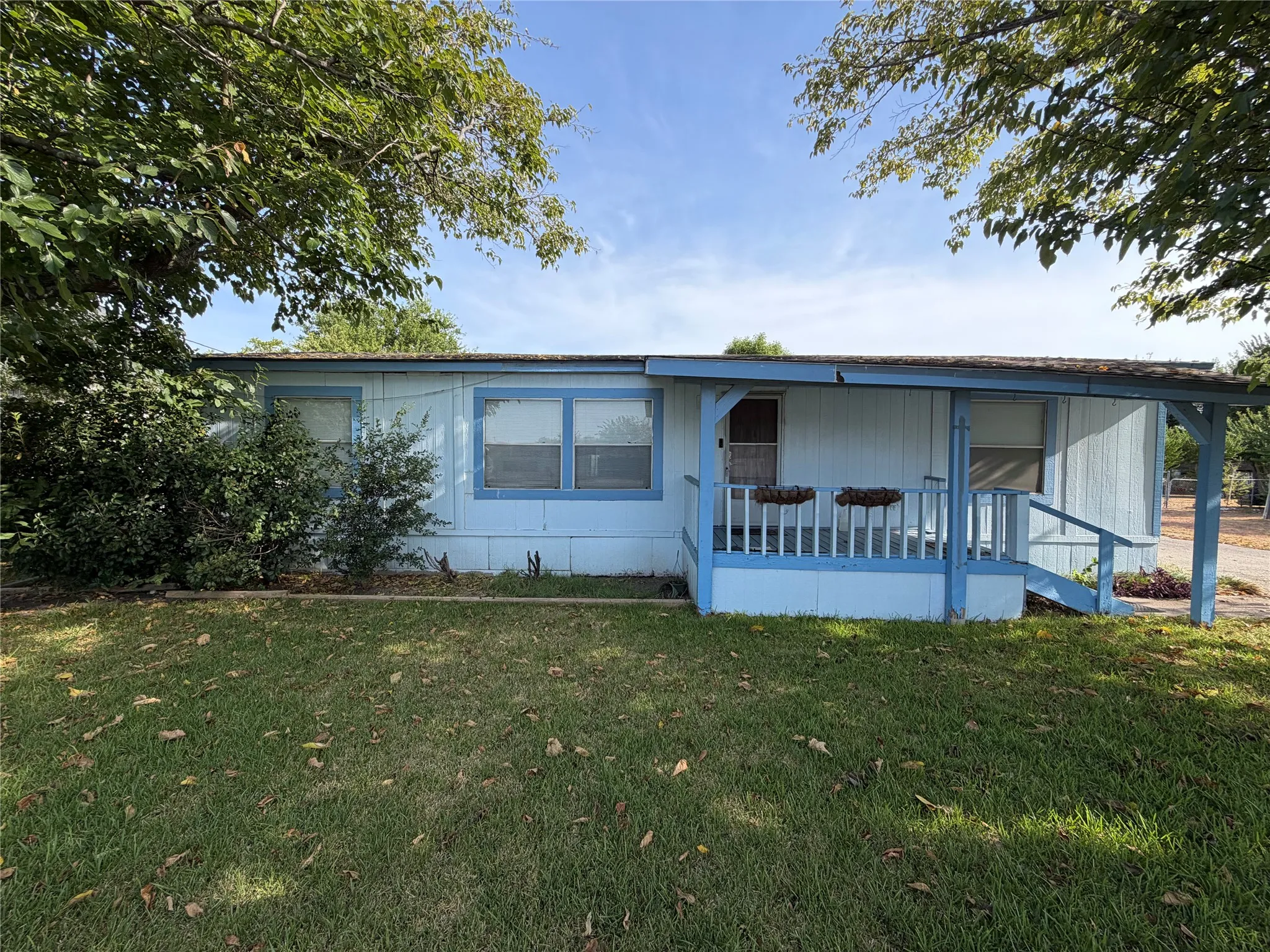 Front exterior with light blue siding, a covered porch, and a grassy yard