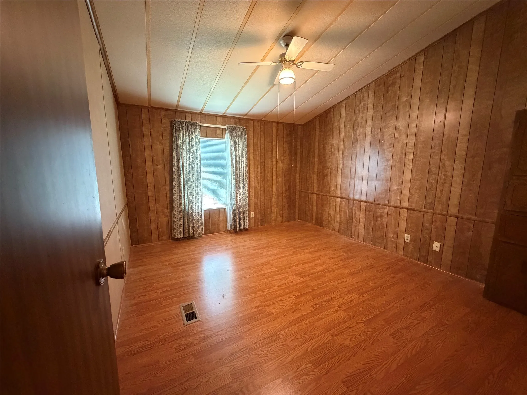 Spacious room featuring warm wood-finish flooring, wood-paneled walls, and a ceiling fan with recessed lighting