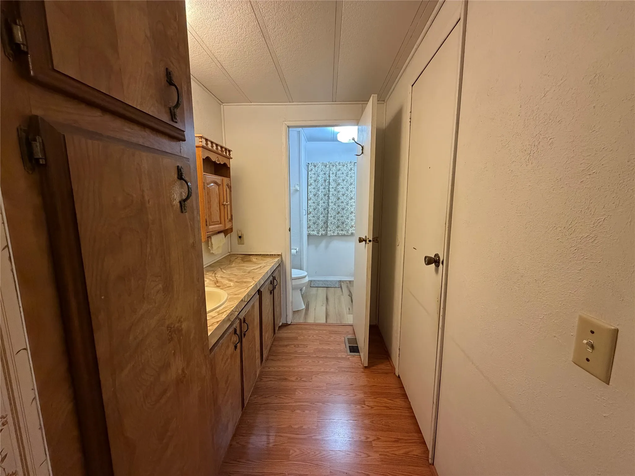 Wood-finish flooring, wood cabinetry with decorative handles, built-in vanity with integrated sink, and overhead wood storage cabinet