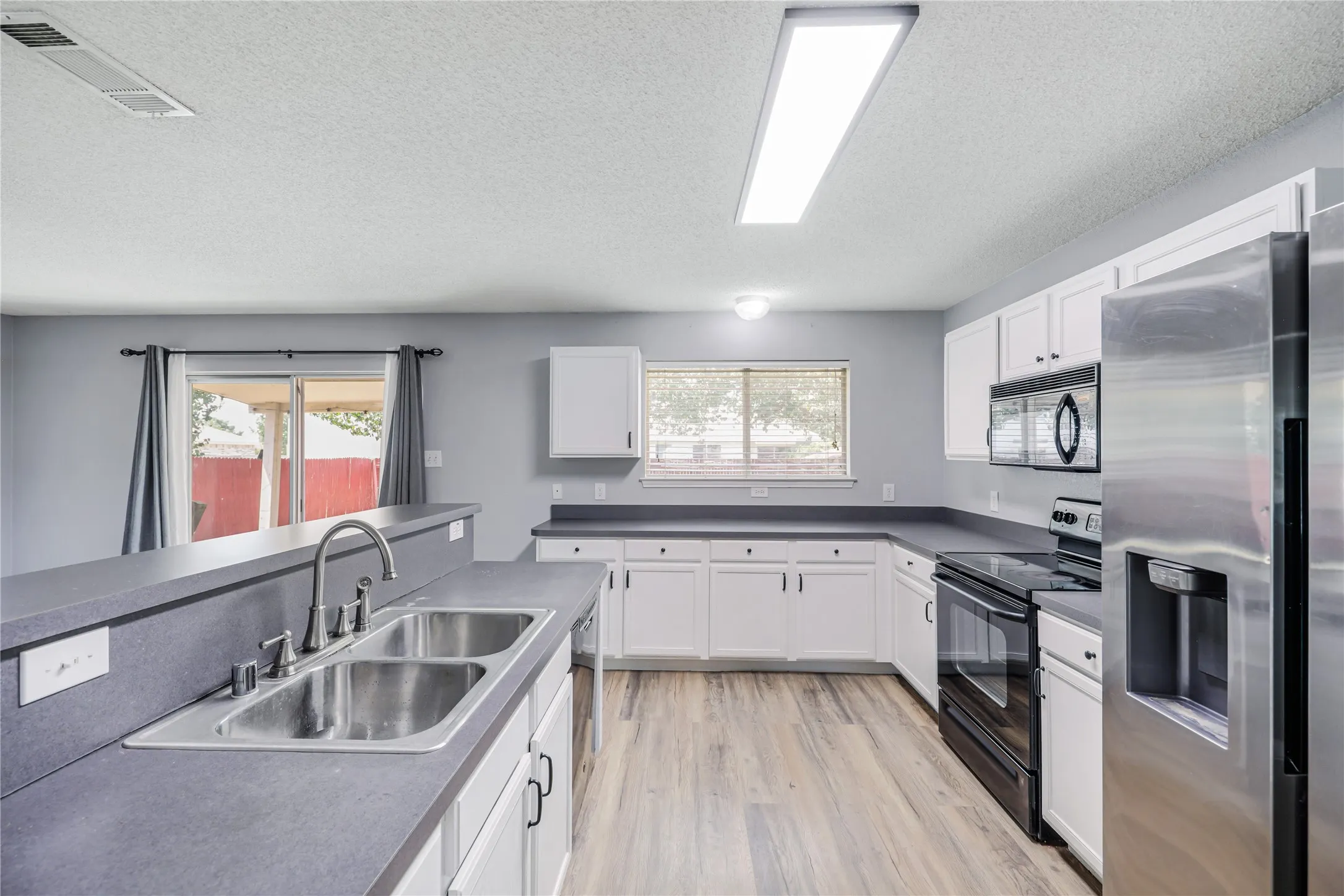 Stainless sink, built-in microwave, glass top range, and a stainless refrigerator featured in this well laid out kitchen