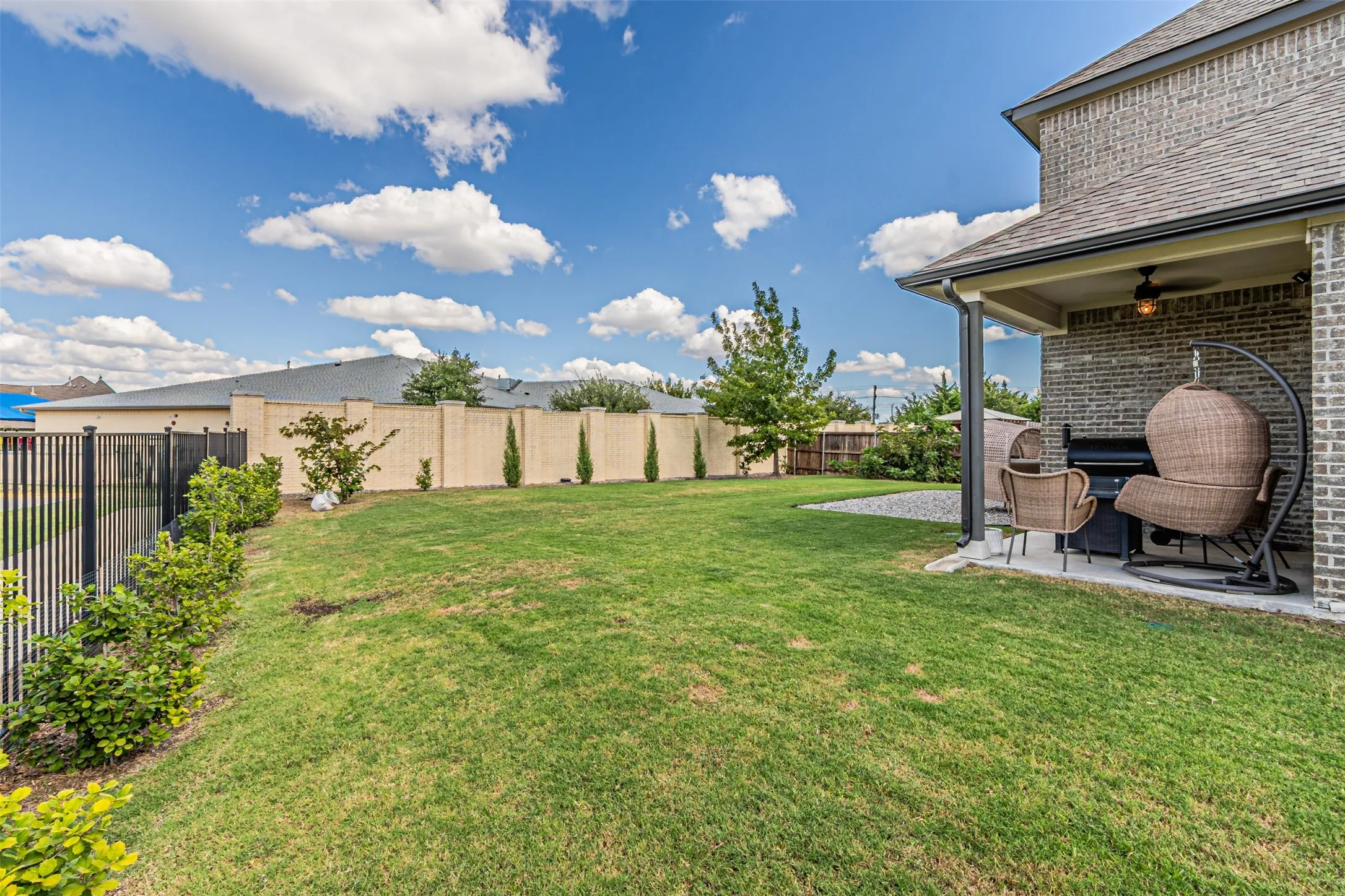 Expansive grass lawn with mature shrubbery and a covered patio featuring a built-in ceiling fan