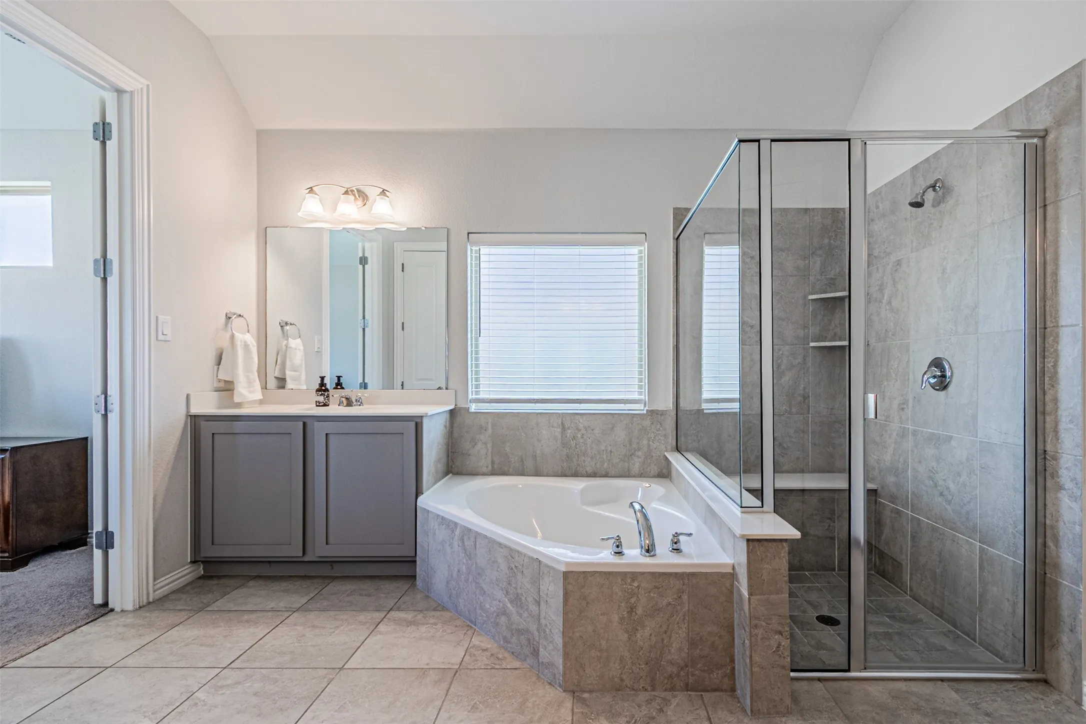 Tiled flooring throughout, corner soaking tub with deck-mounted fixtures, and a glass-enclosed shower with tiled walls