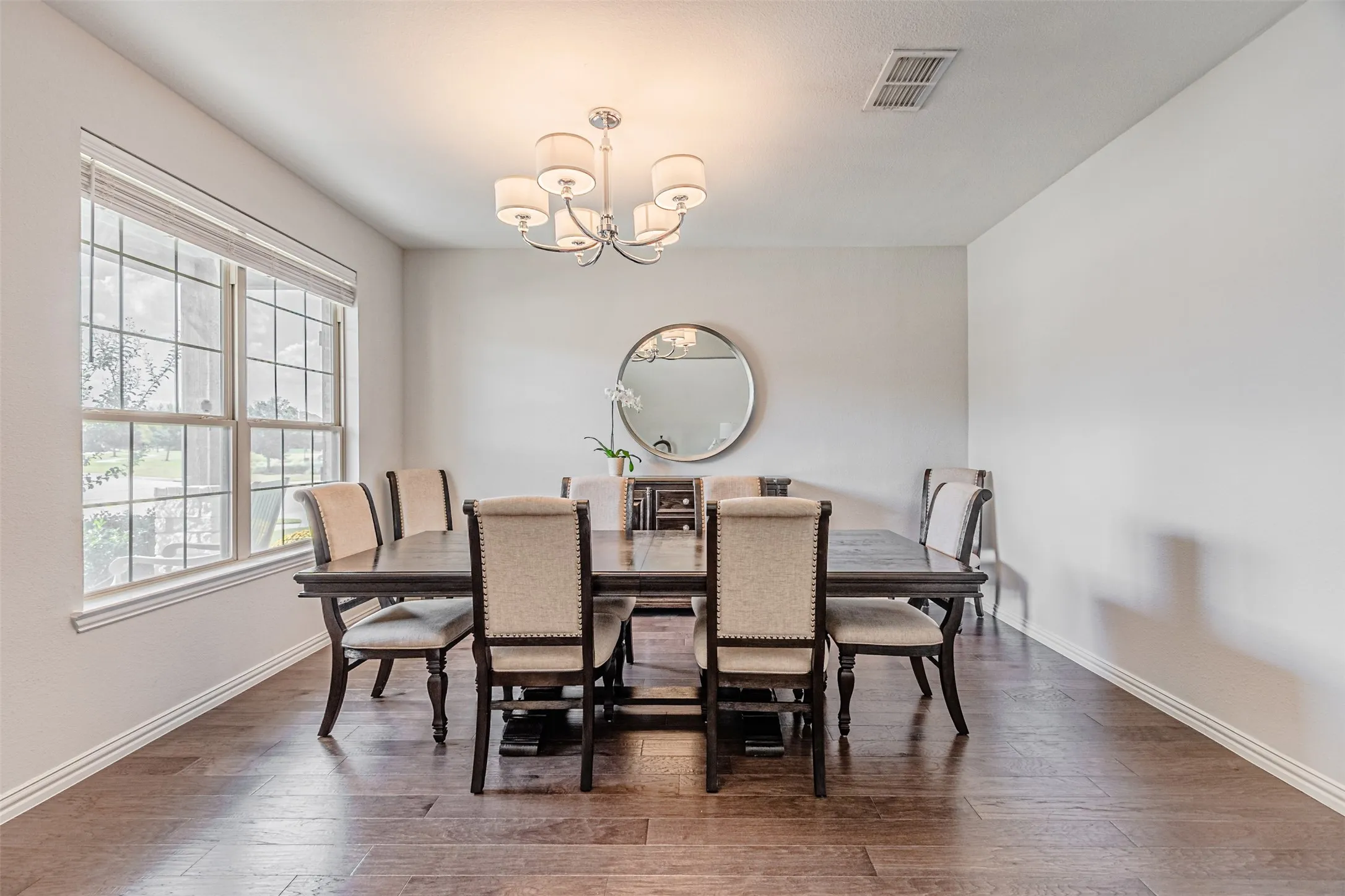 Wood-finish flooring, large window with blinds, and a drum-shade chandelier