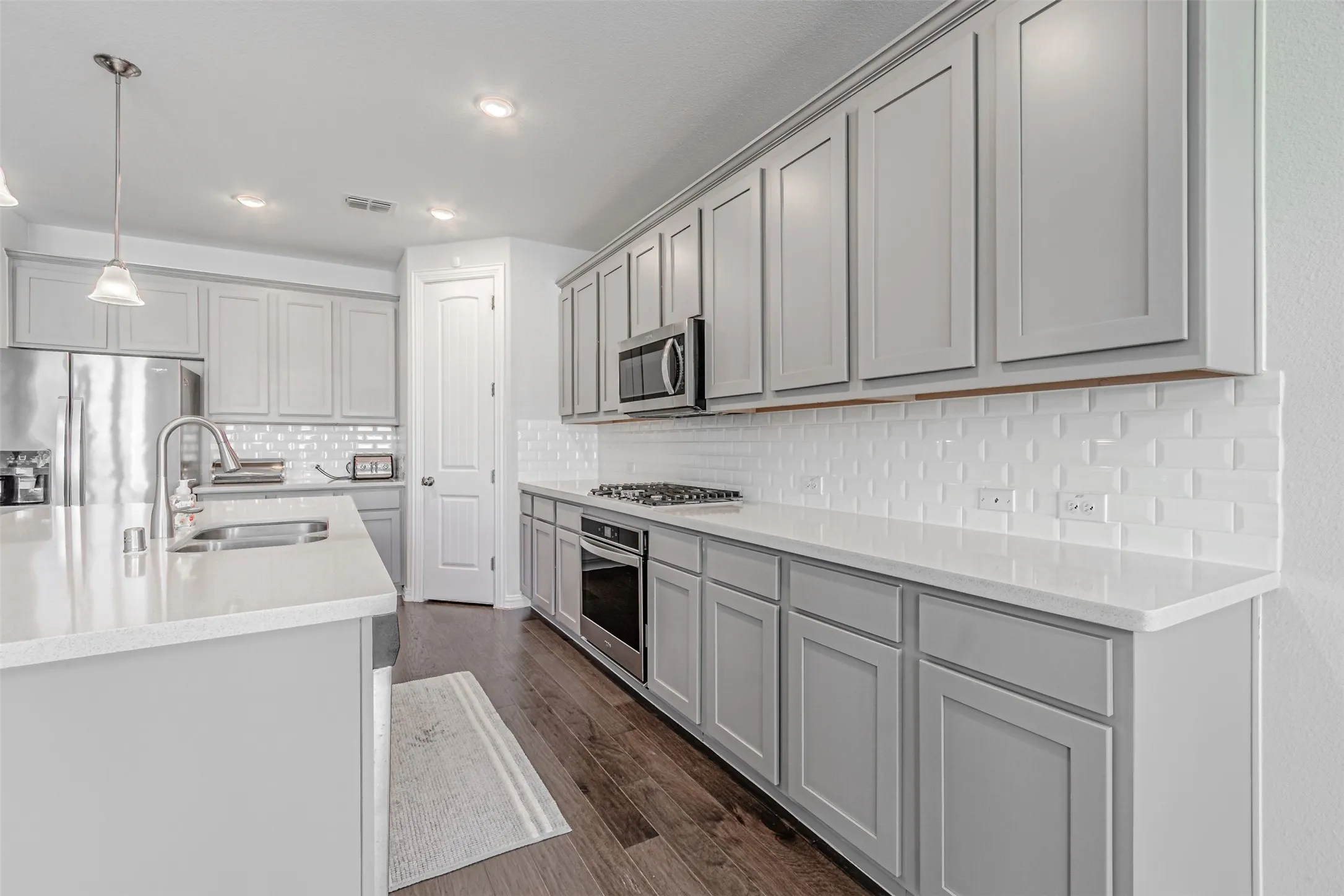 Kitchen featuring wood-finish flooring, light gray cabinetry, white subway tile backsplash, white countertops, and stainless steel appliances