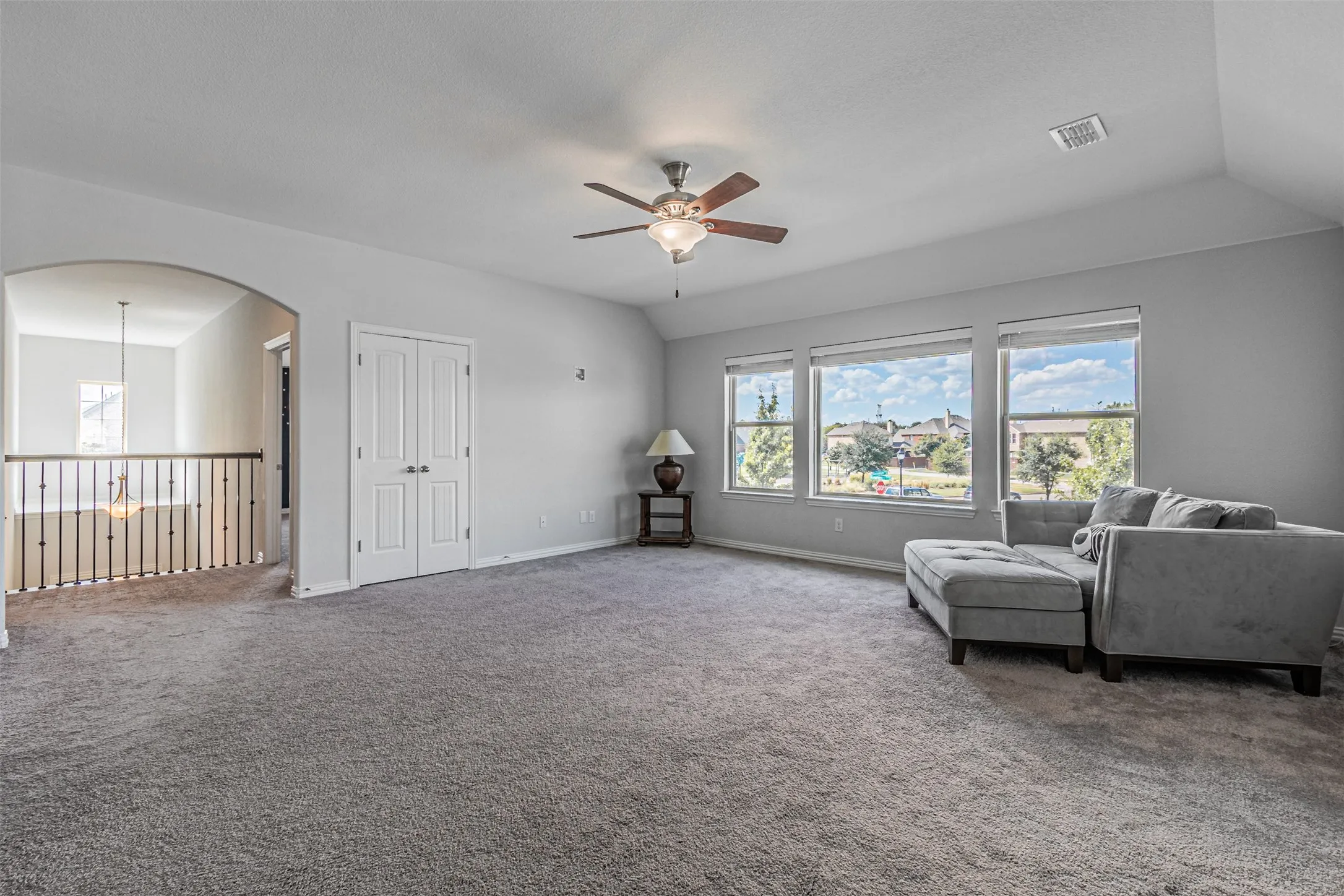 Spacious upper-level room featuring gray carpeting, multiple large windows, a ceiling fan, and white double doors