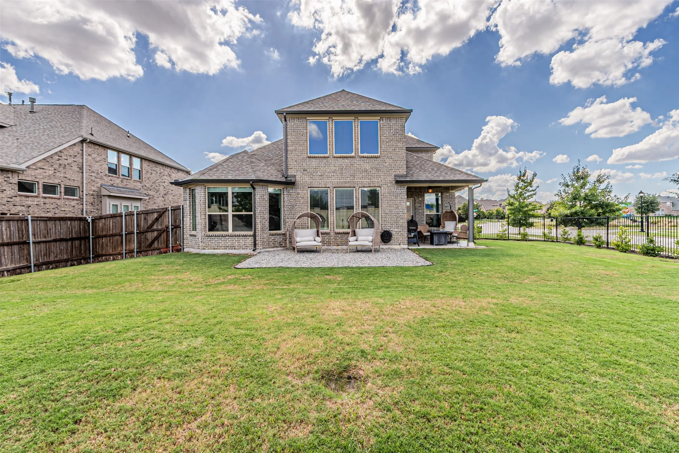 Brick exterior with multiple windows, covered patio, gravel patio area, and a spacious lawn