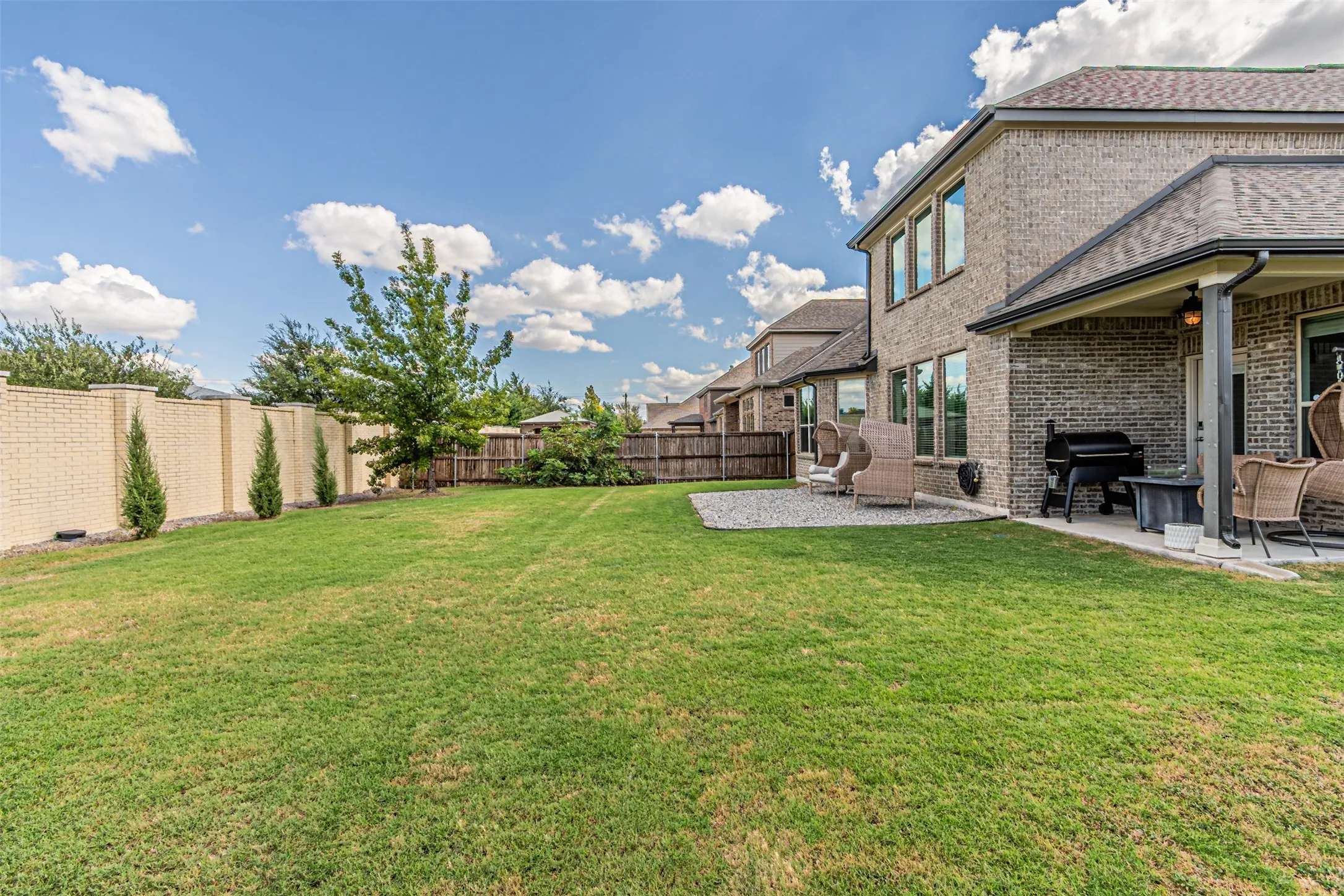 Expansive lawn area with a covered patio, brick exterior, and a privacy fence