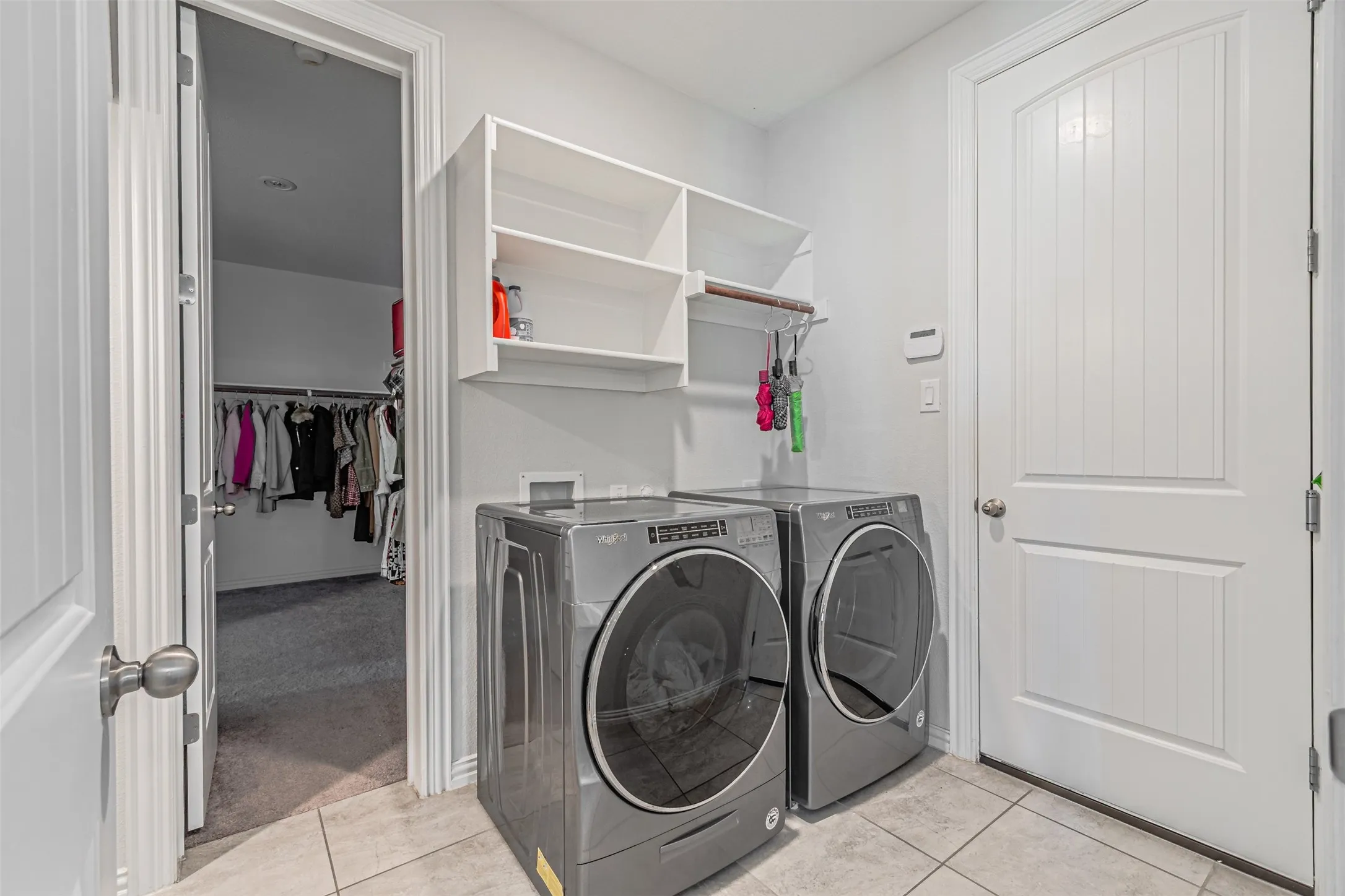 Laundry area featuring tile flooring, white shelving, and a built-in hanging rod
