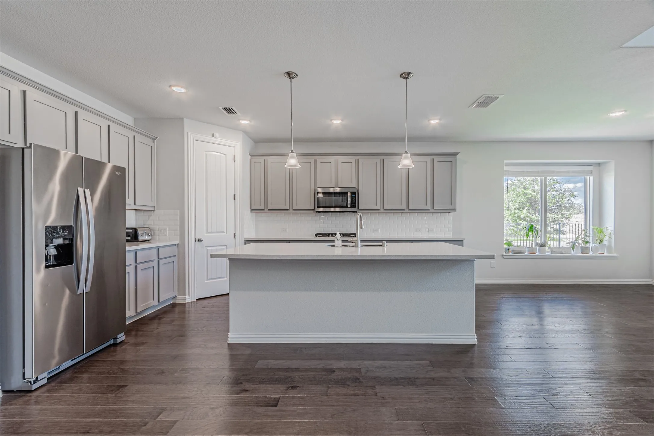 Kitchen featuring wood-finish flooring, light gray cabinetry, stainless steel appliances, a center island with pendant lighting, and a white tile backsplash