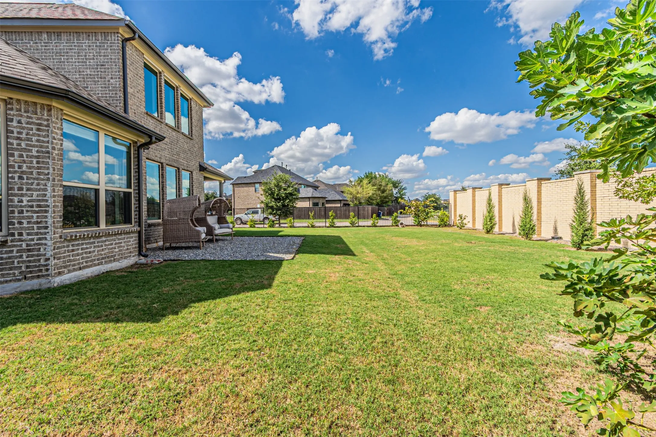 Expansive lawn area with a stone-finish privacy wall, gravel patio, and multiple windows