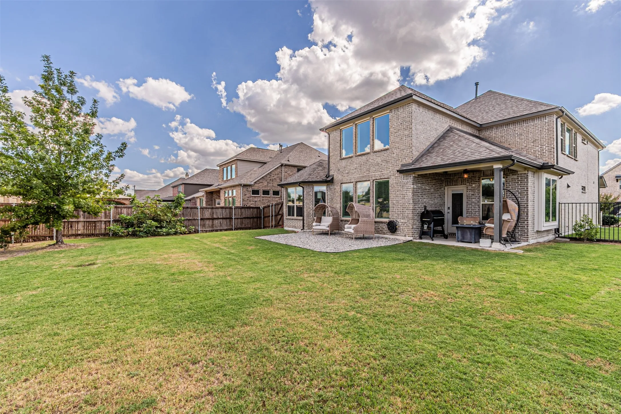 Expansive backyard featuring a covered patio, gravel patio, privacy fencing, and multiple windows