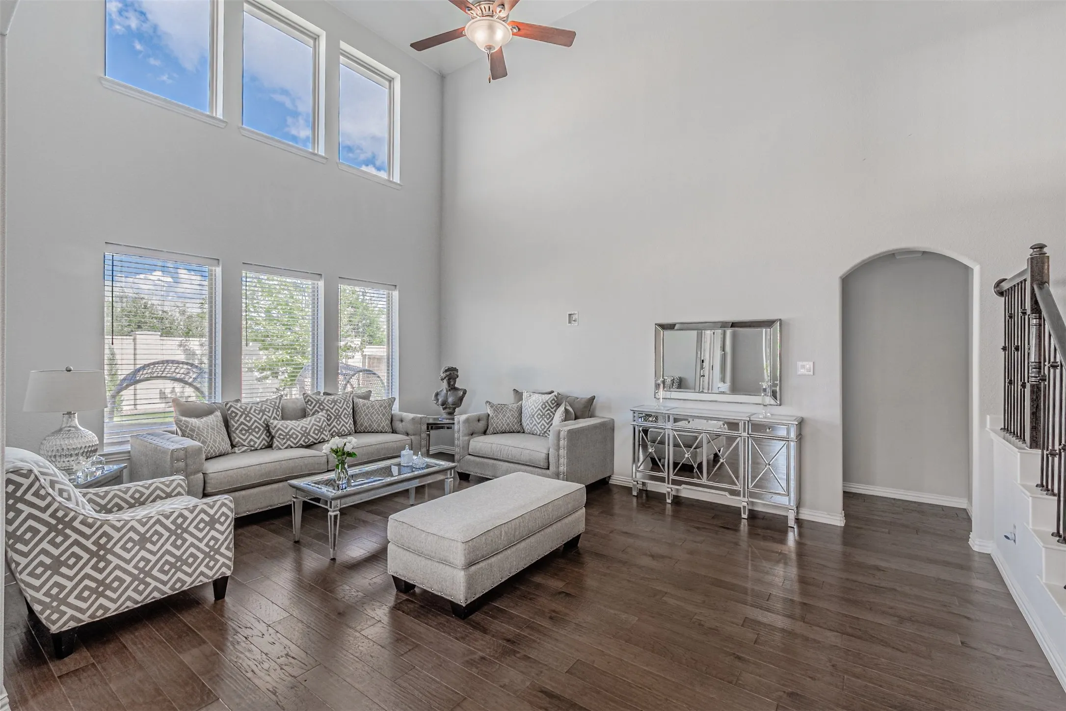 Two-story living area with high ceilings, dark wood-finish flooring, and a ceiling fan
