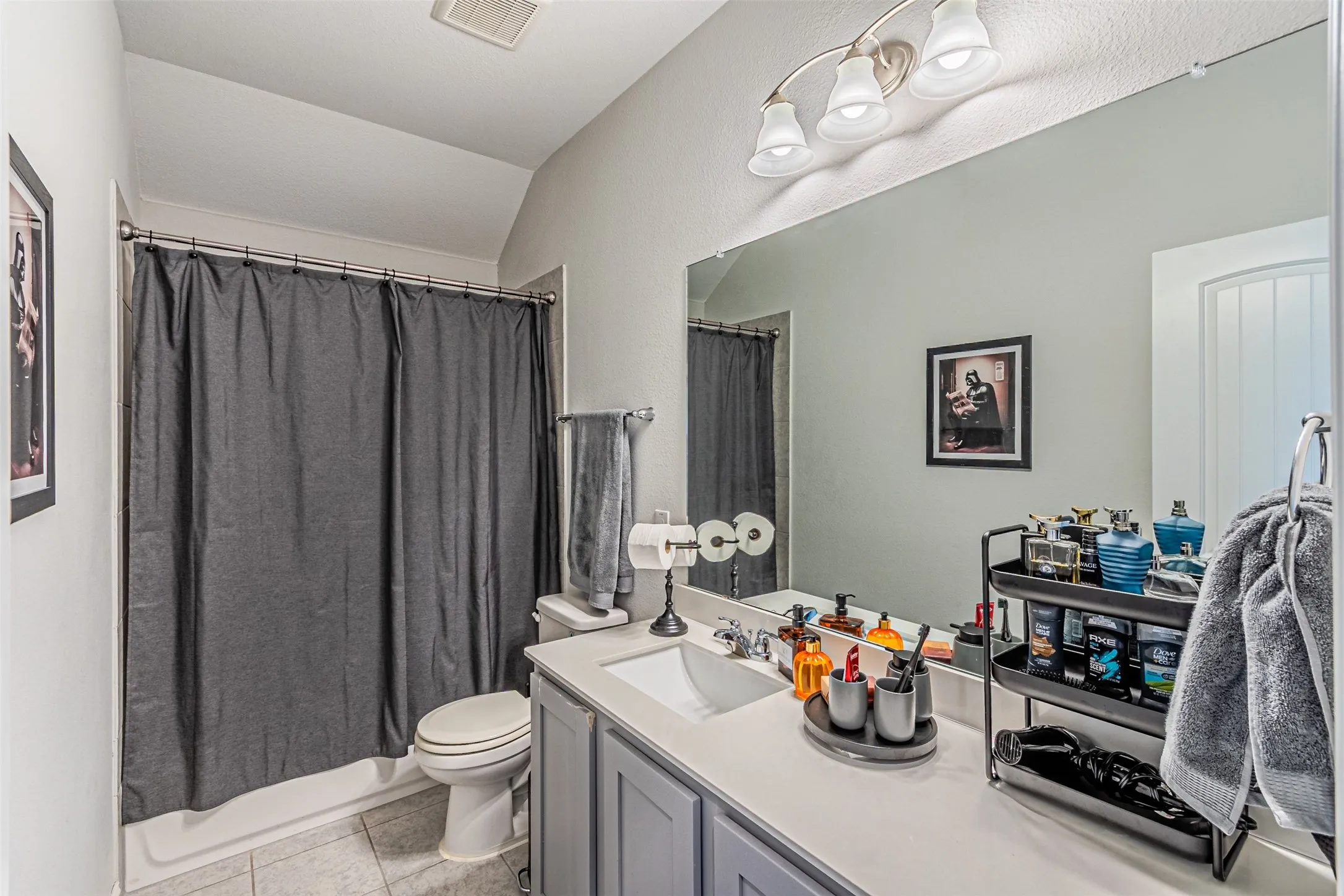 Bathroom featuring a shower-tub combination, single vanity with light-colored countertop, large wall-mounted mirror, and tile flooring