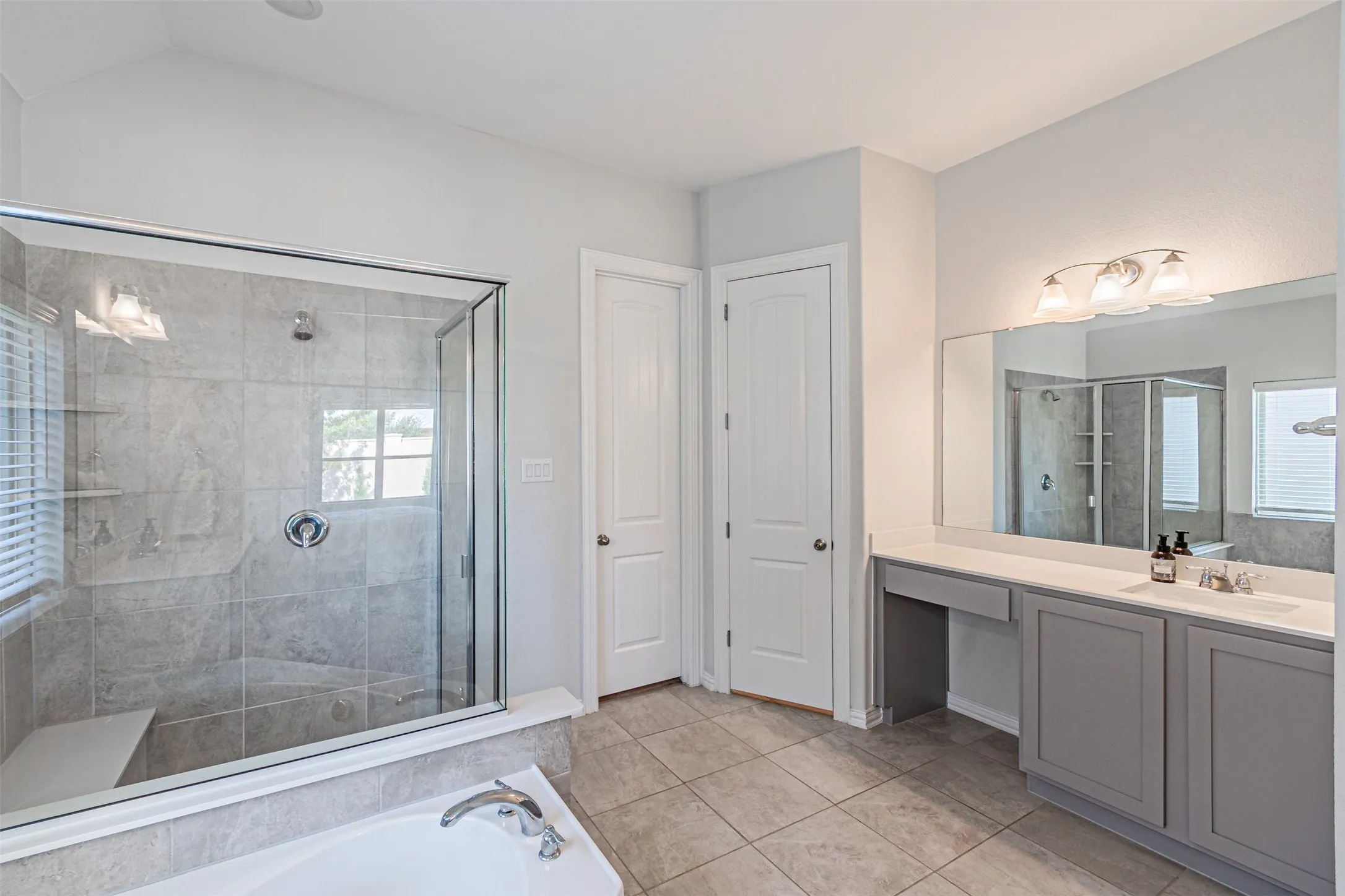 Spacious bathroom featuring a glass-enclosed shower with a built-in bench, a separate bathtub, and a double vanity with a makeup area