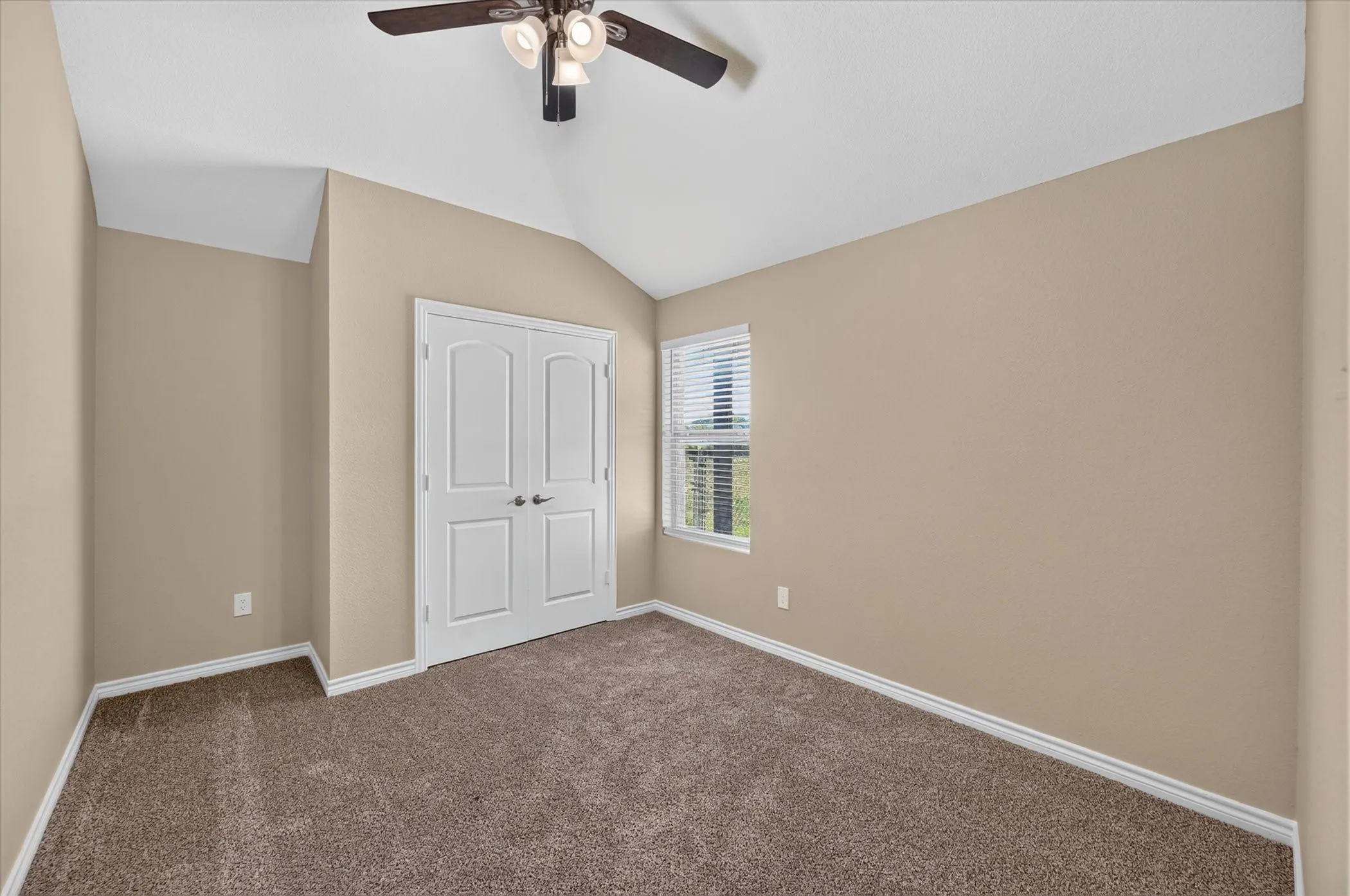 Vaulted ceiling with a ceiling fan, plush carpet flooring, and a double-door closet