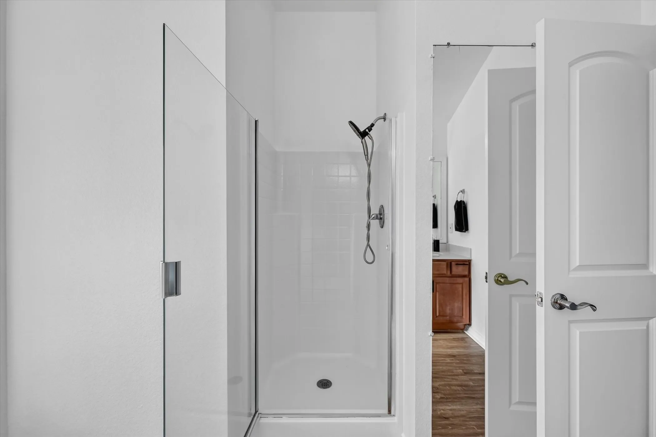 Glass-enclosed shower with white tiled walls and a handheld showerhead