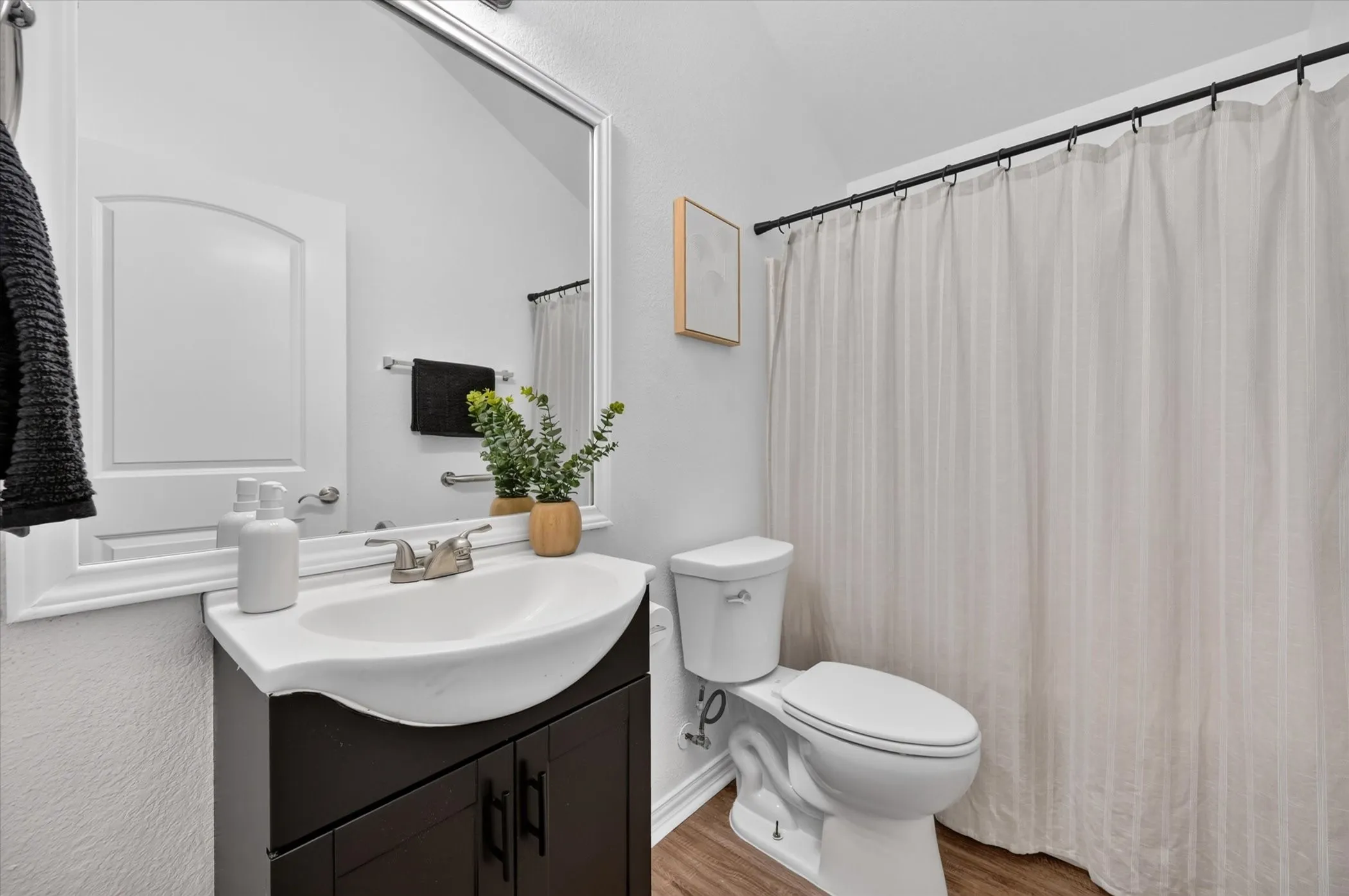 Wood-finish flooring with a dark wood-finish vanity, integrated white sink, and framed mirror