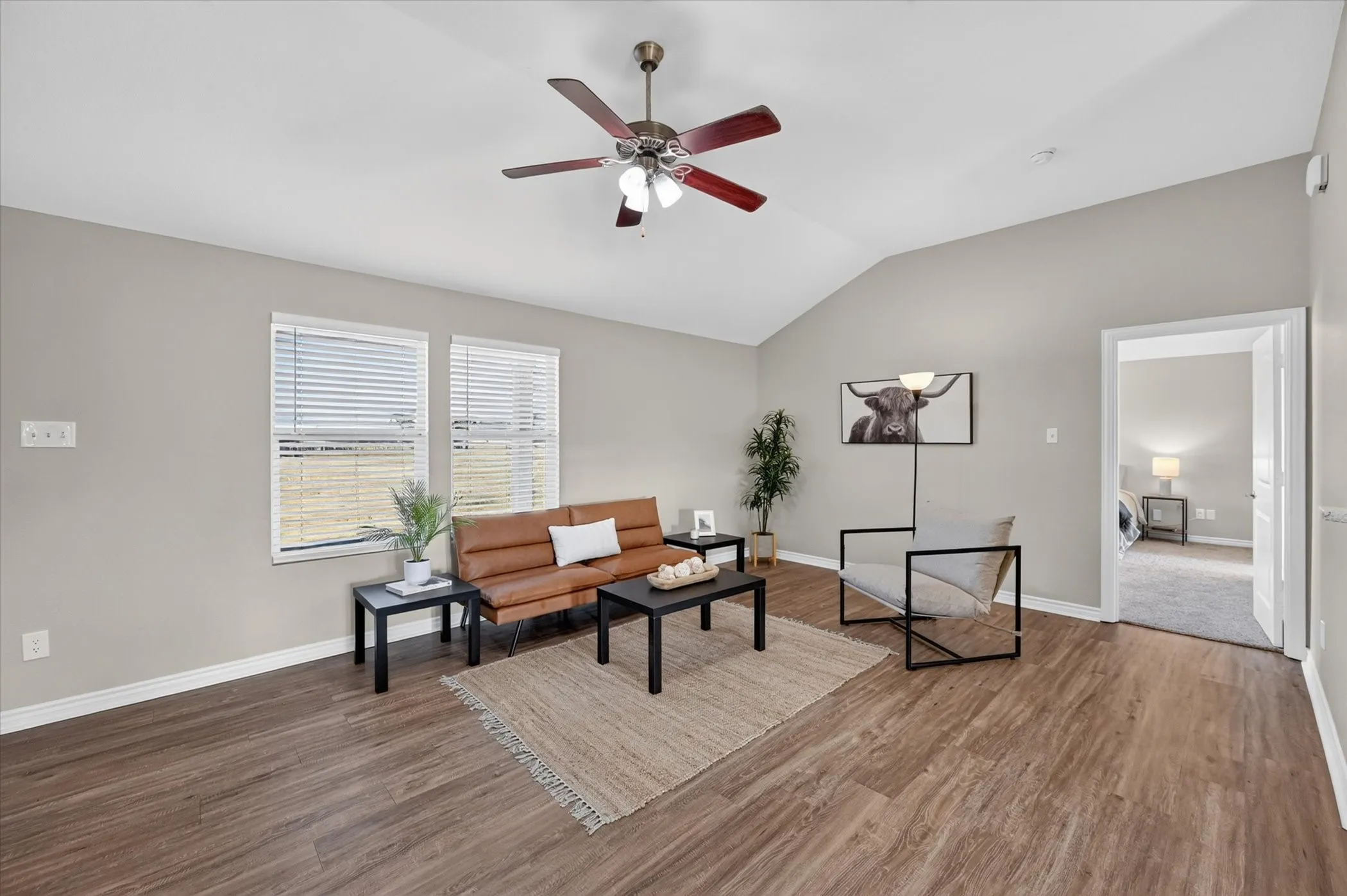 Vaulted ceiling with a ceiling fan, dual windows with blinds, and wood-finish flooring
