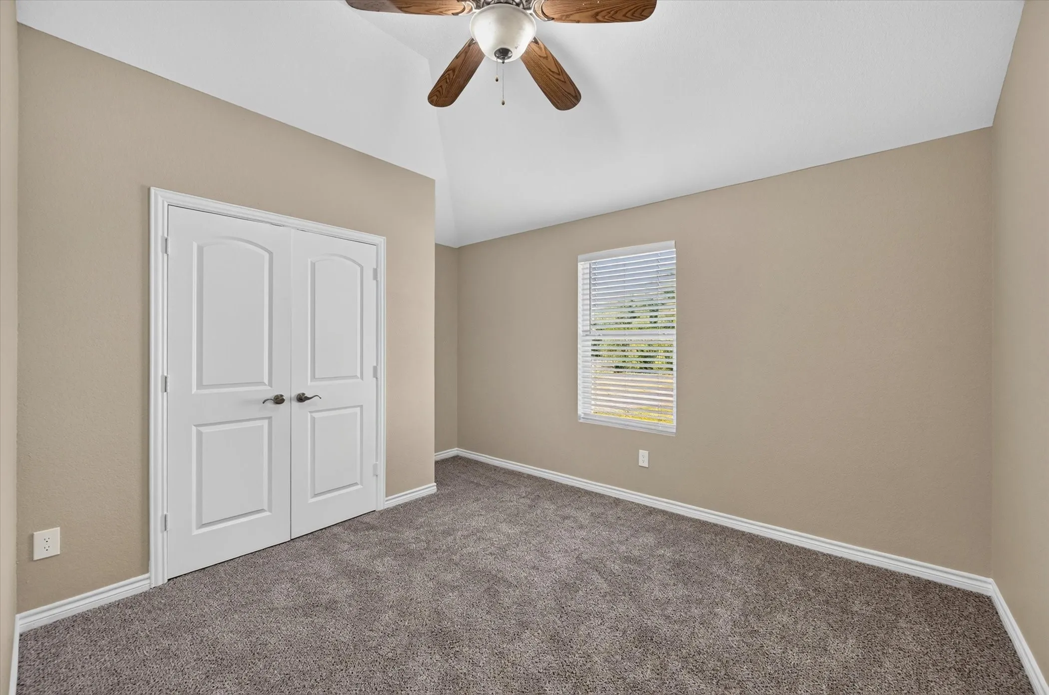 Vaulted ceiling with wood-finish ceiling fan, neutral wall tones, window with blinds, and plush carpet flooring
