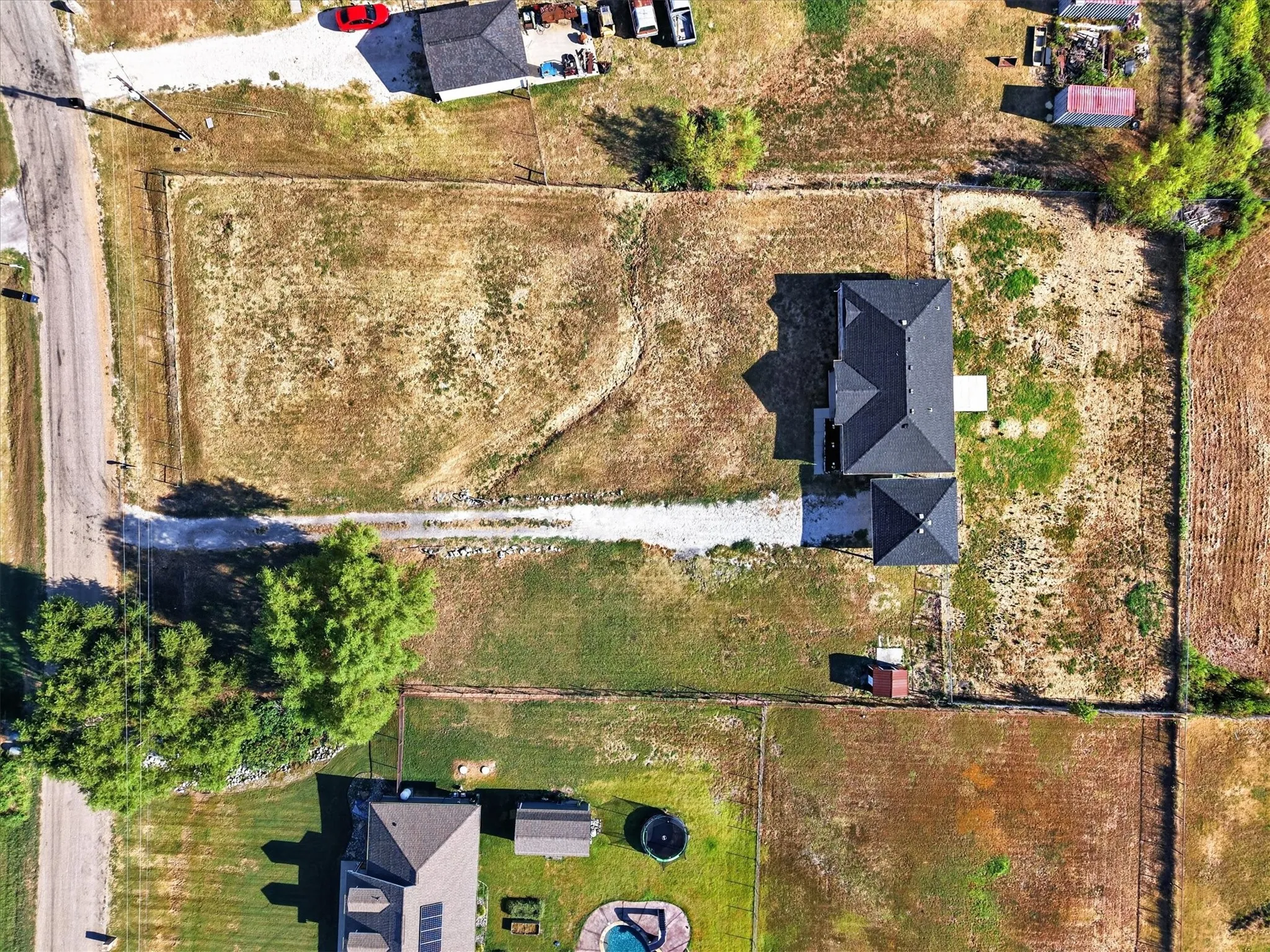 New construction residence featuring a dark shingled roof, a gravel driveway, and surrounding undeveloped land