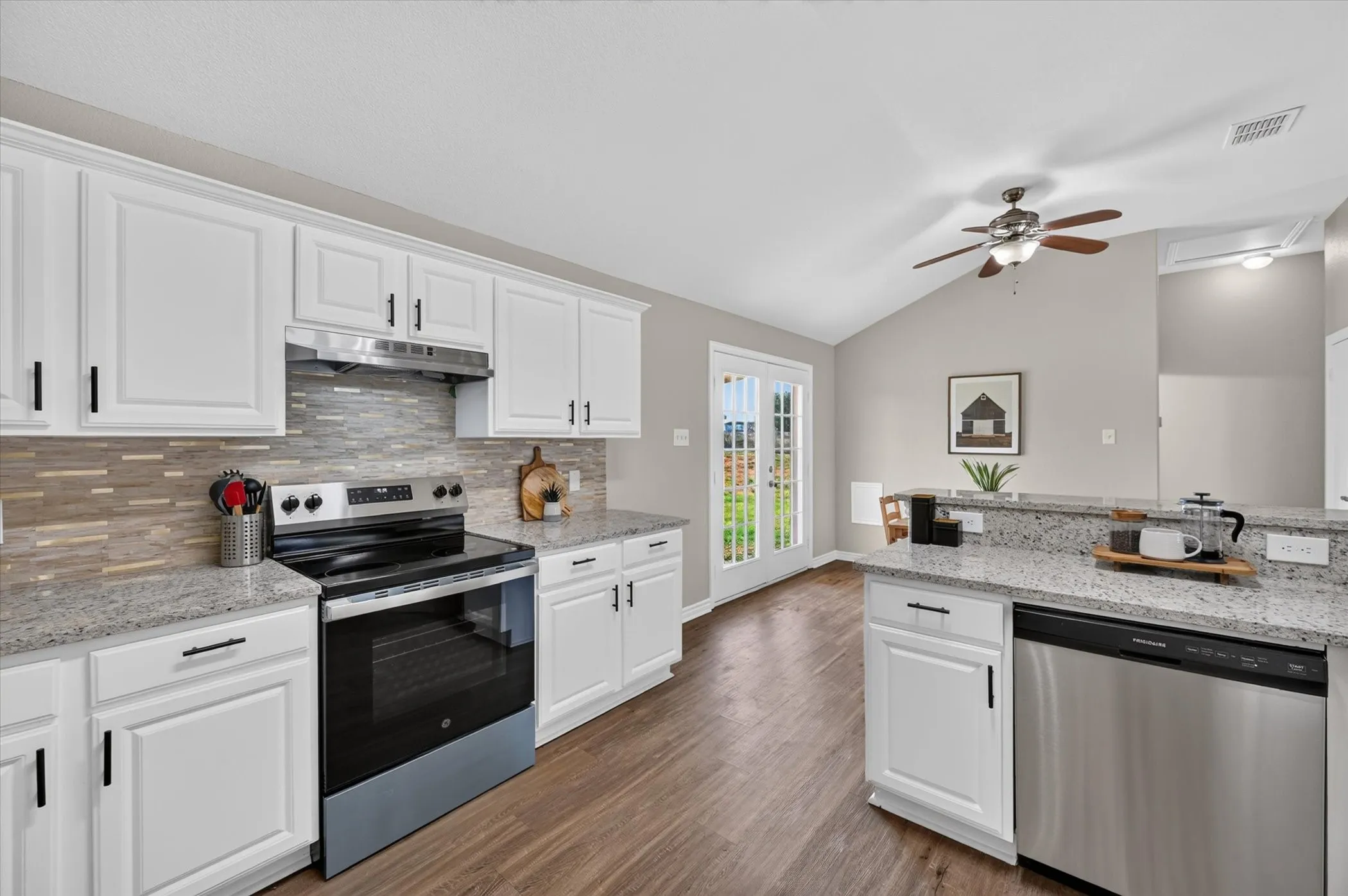 Kitchen featuring white shaker-style cabinetry, stainless steel appliances, speckled countertops, and wood-finish flooring