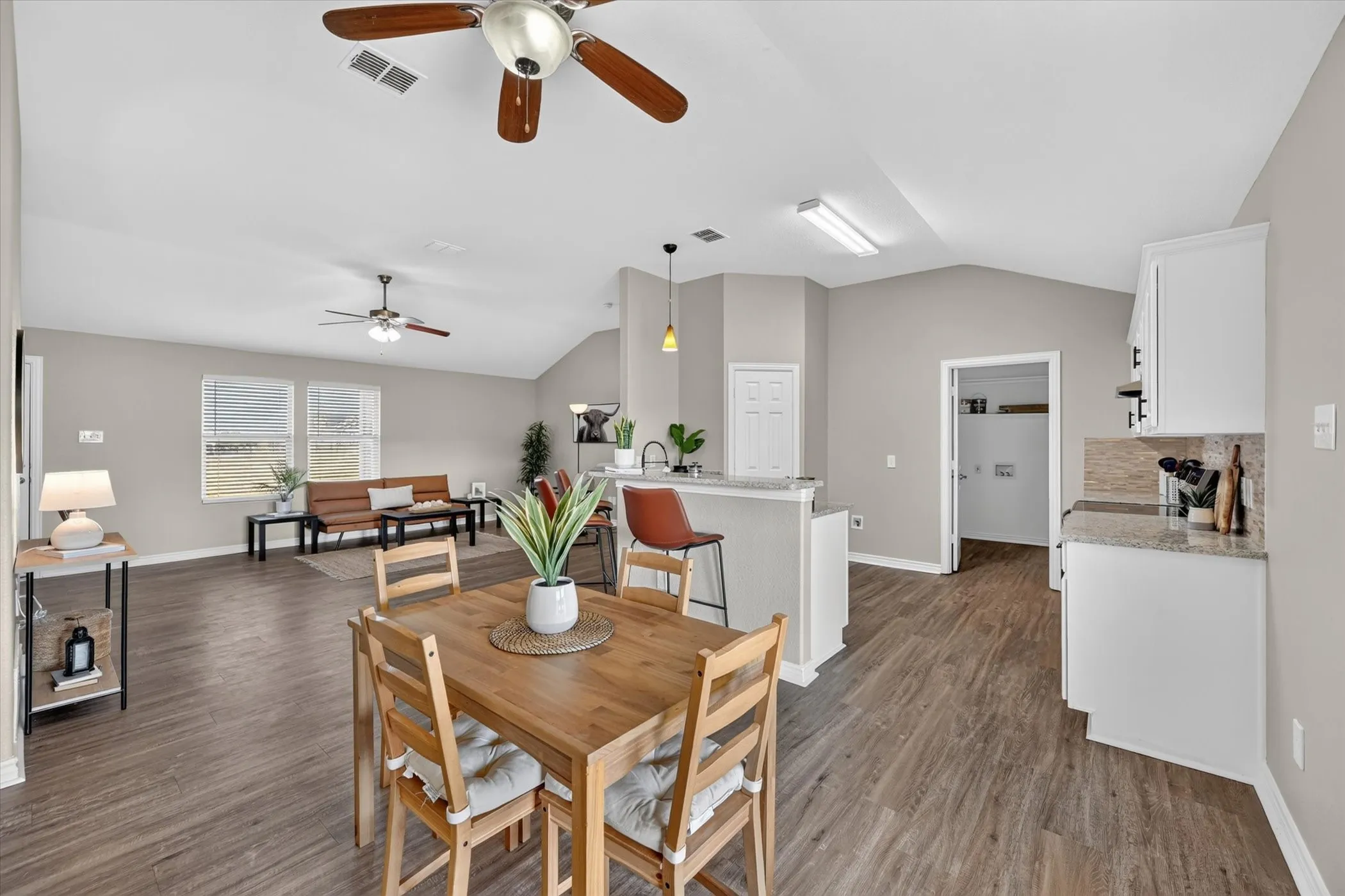 Vaulted ceilings, wood-finish flooring, white cabinetry, granite-finish countertops, and a tile backsplash