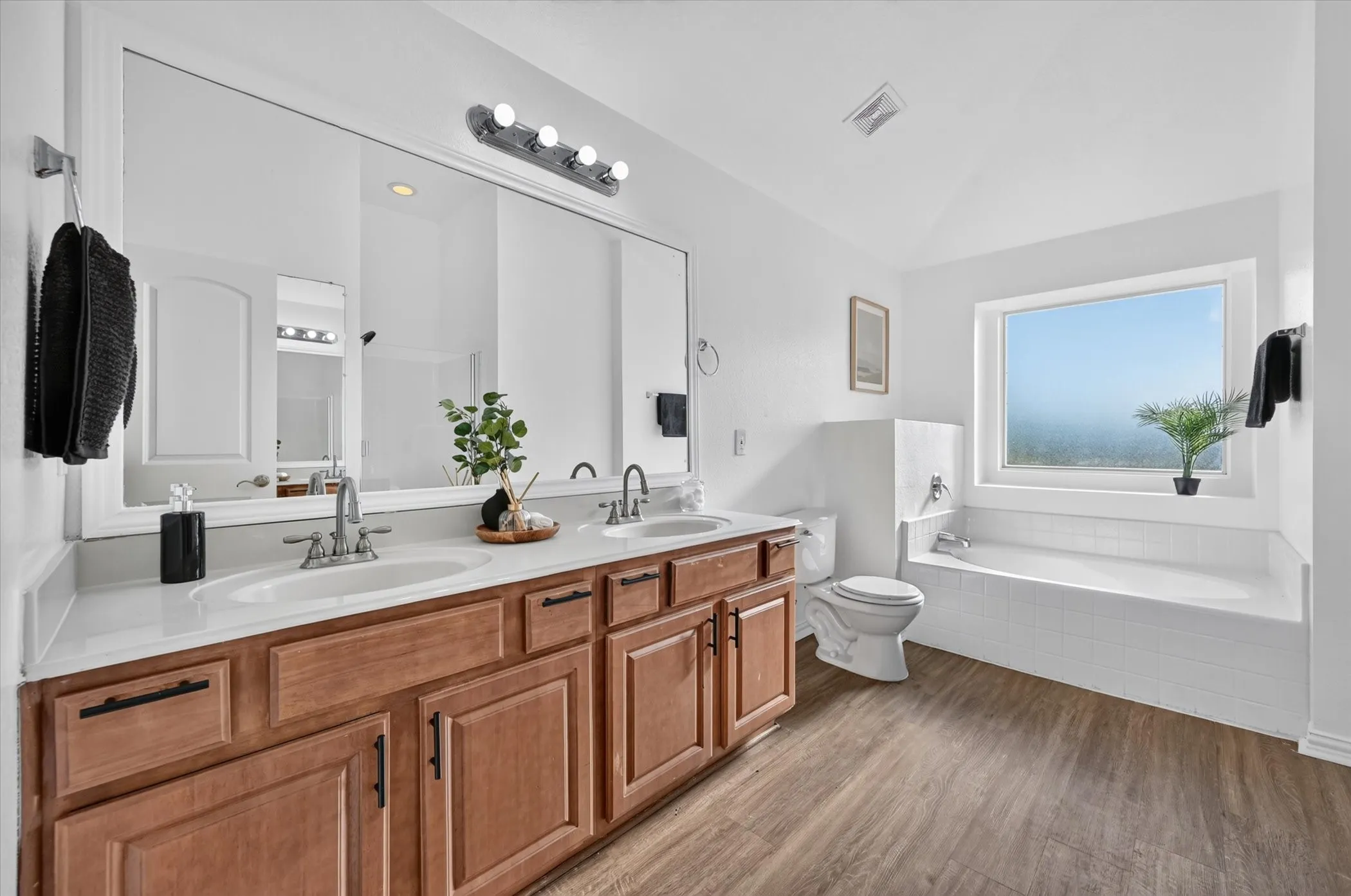 Spa-inspired primary bathroom featuring a wood-finish vanity with multiple storage drawers, white quartz countertop, and dual sinks with polished chrome fixtures