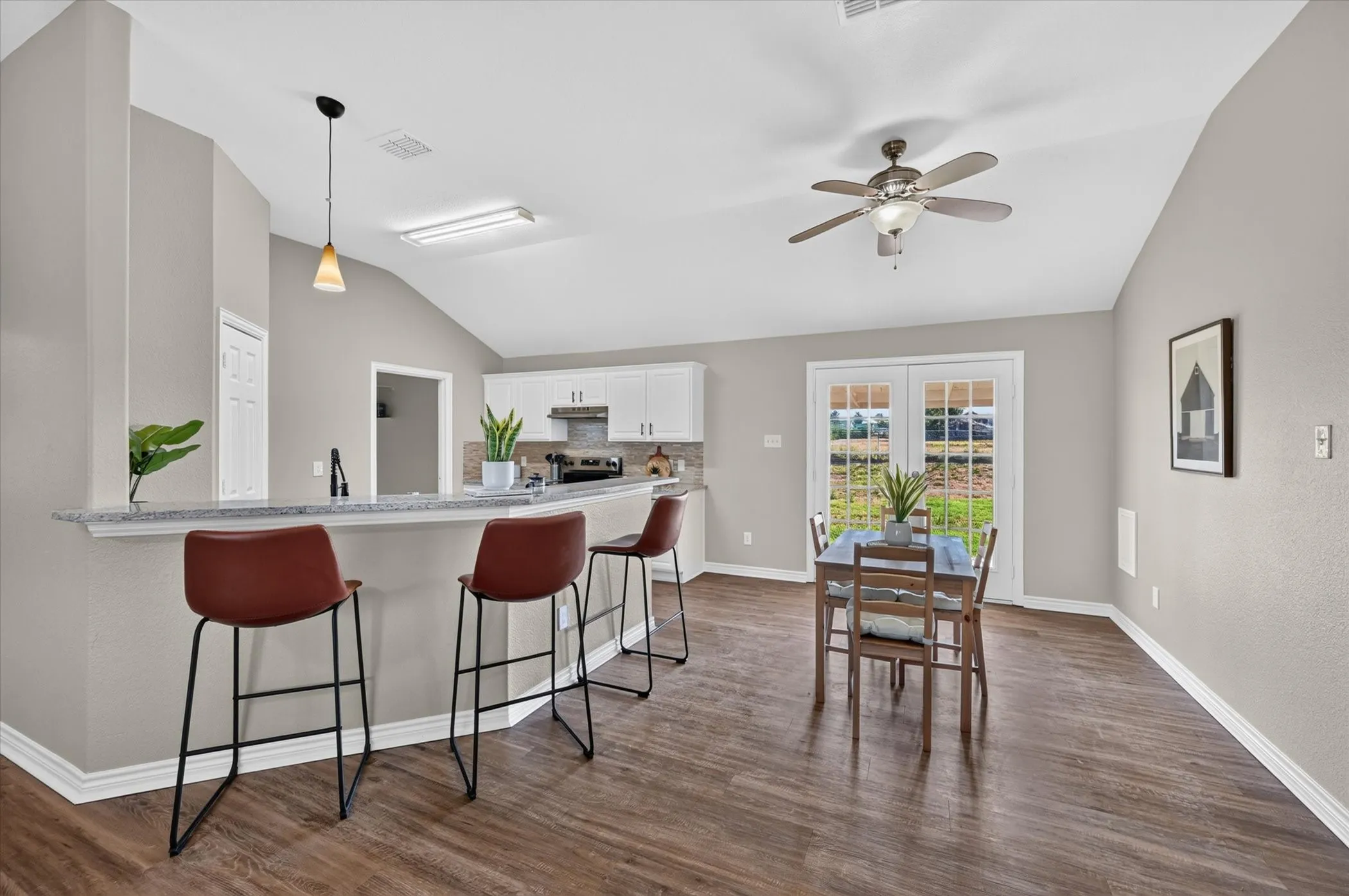 Vaulted ceiling, wood-finish flooring, kitchen with peninsula seating, white cabinetry, and French doors