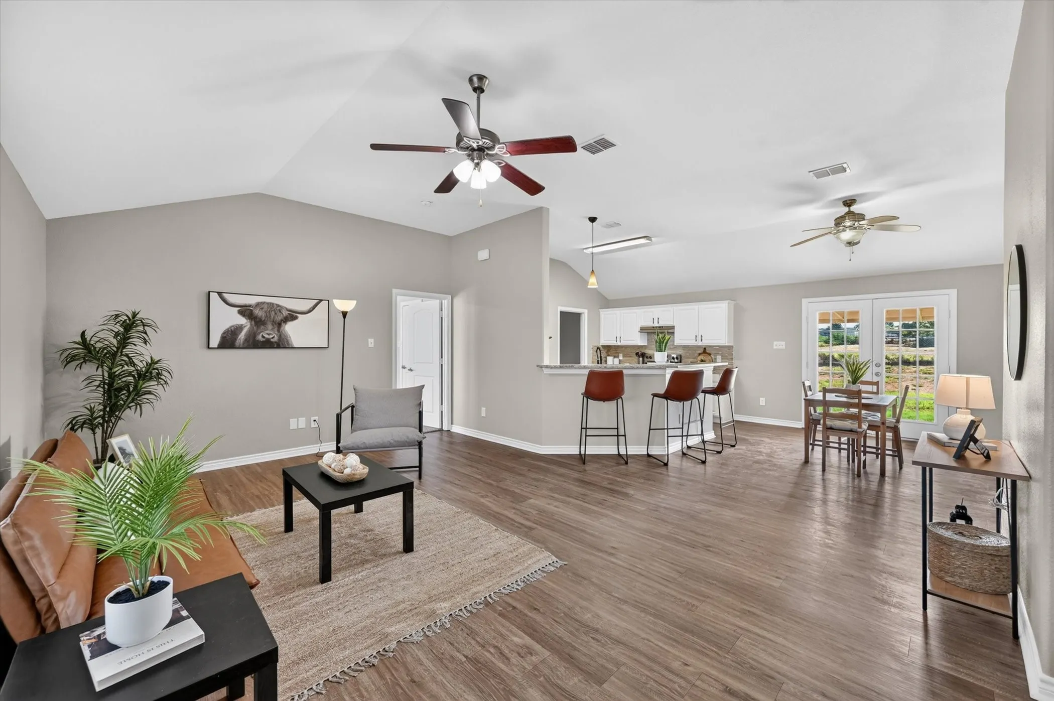 Vaulted ceilings with ceiling fans, wood-finish flooring, white kitchen cabinetry, and French doors