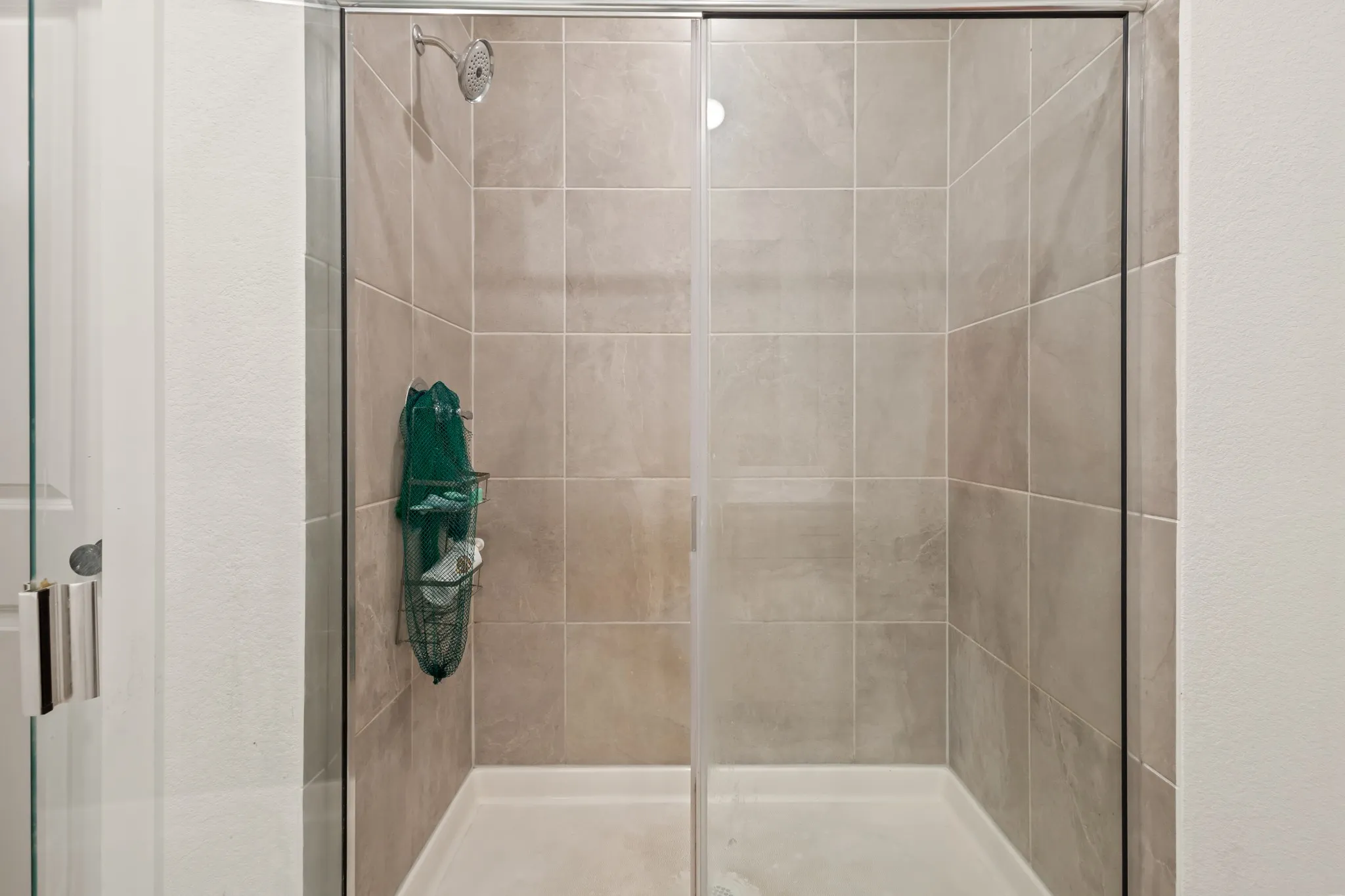 Glass-enclosed shower with a tiled surround, a built-in showerhead, and a white shower pan