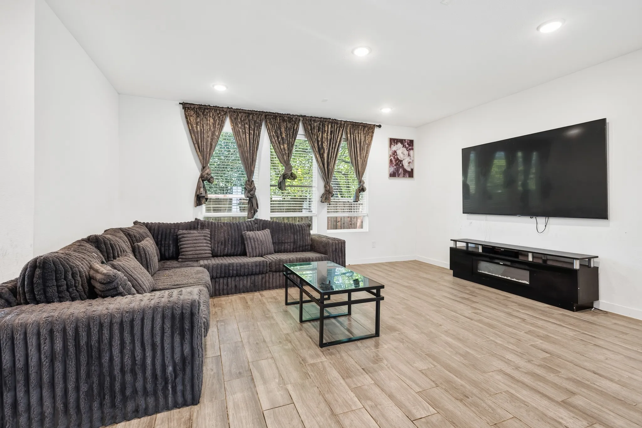 Recessed lighting illuminates the room, featuring wood-finish flooring and multiple windows