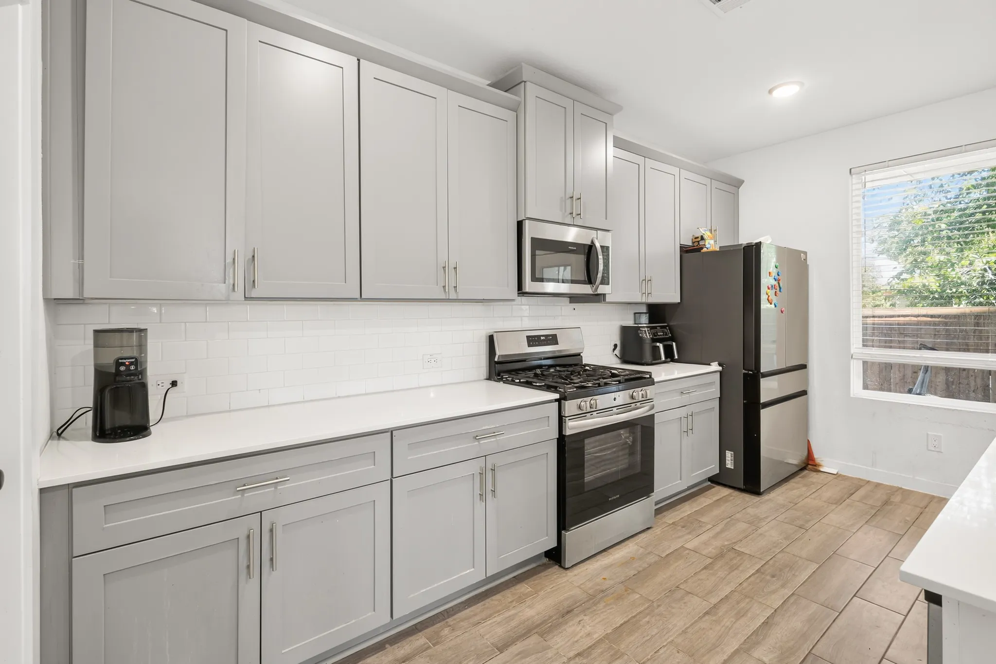 Kitchen featuring light gray cabinetry, white subway tile backsplash, stainless steel appliances, and wood-finish flooring