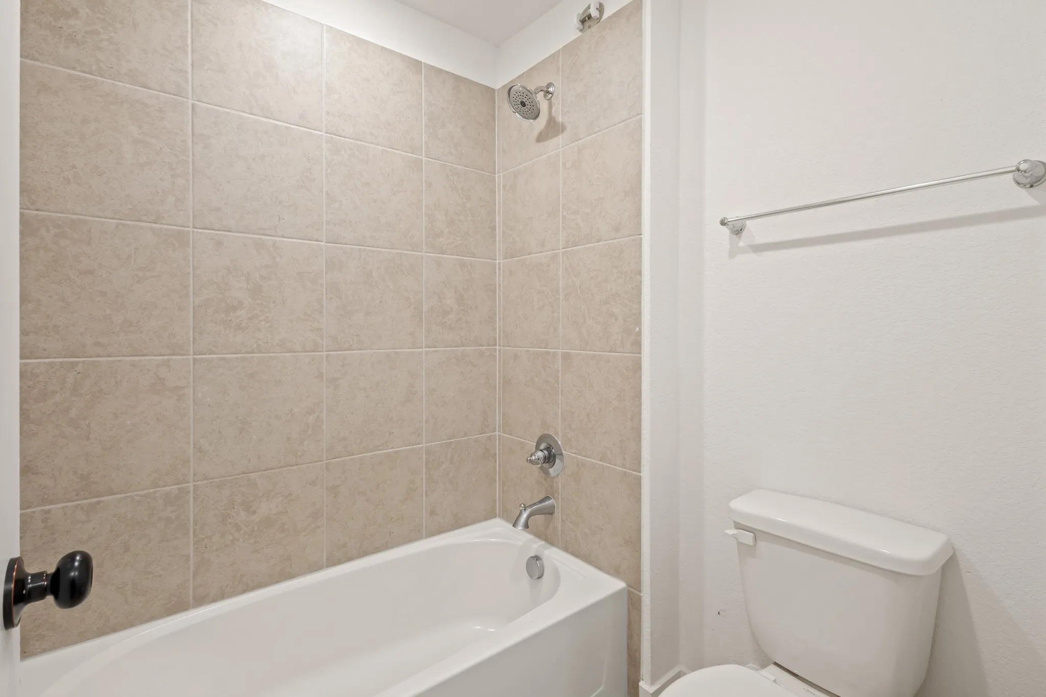 Bathtub with tiled shower surround, chrome fixtures, and a white toilet