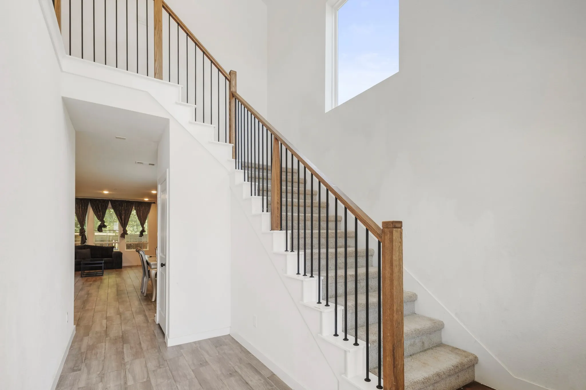 Hardwood-look flooring, carpeted staircase, wrought iron balusters, wood-finish handrail, and high-set window