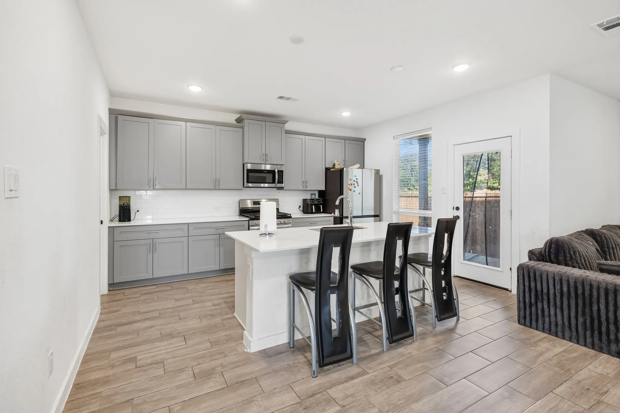 Kitchen featuring gray shaker-style cabinetry, stainless steel appliances, a white subway tile backsplash, and a center island with a white countertop