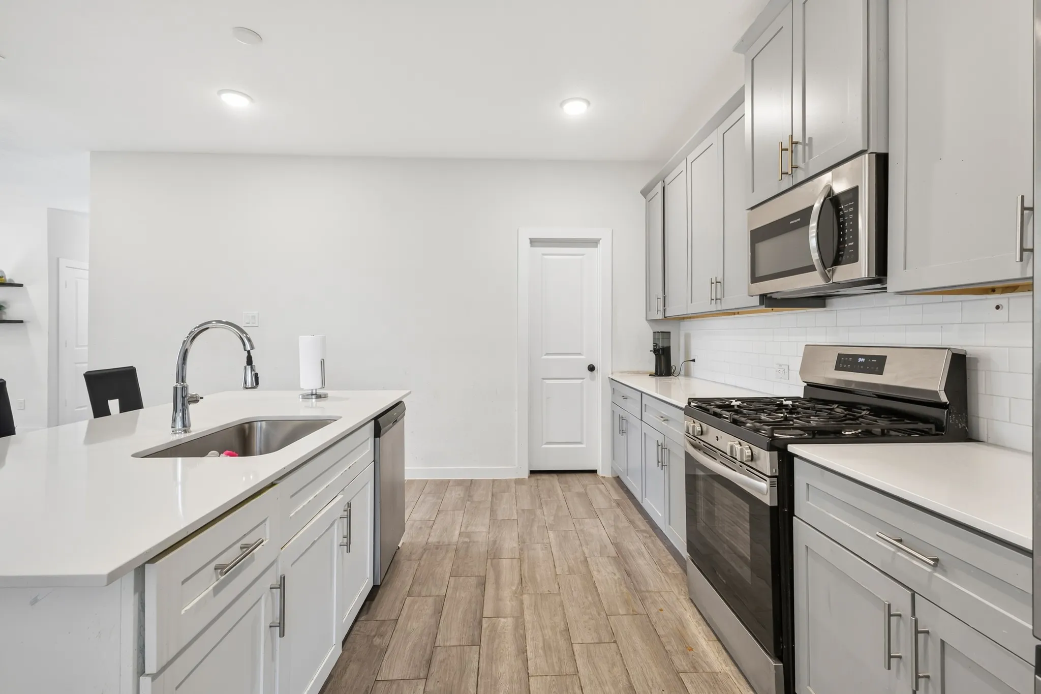 Kitchen featuring an expansive island with an undermount sink, stainless steel appliances, light gray cabinetry, white countertops, and wood-finish flooring