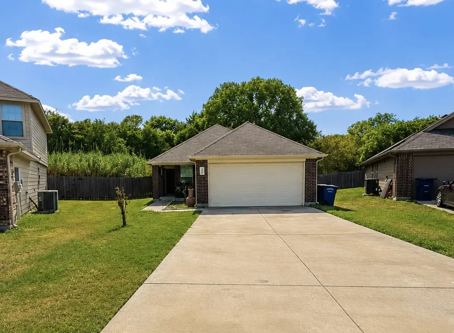 Brick facade, attached garage, concrete driveway, front lawn, and a fenced perimeter